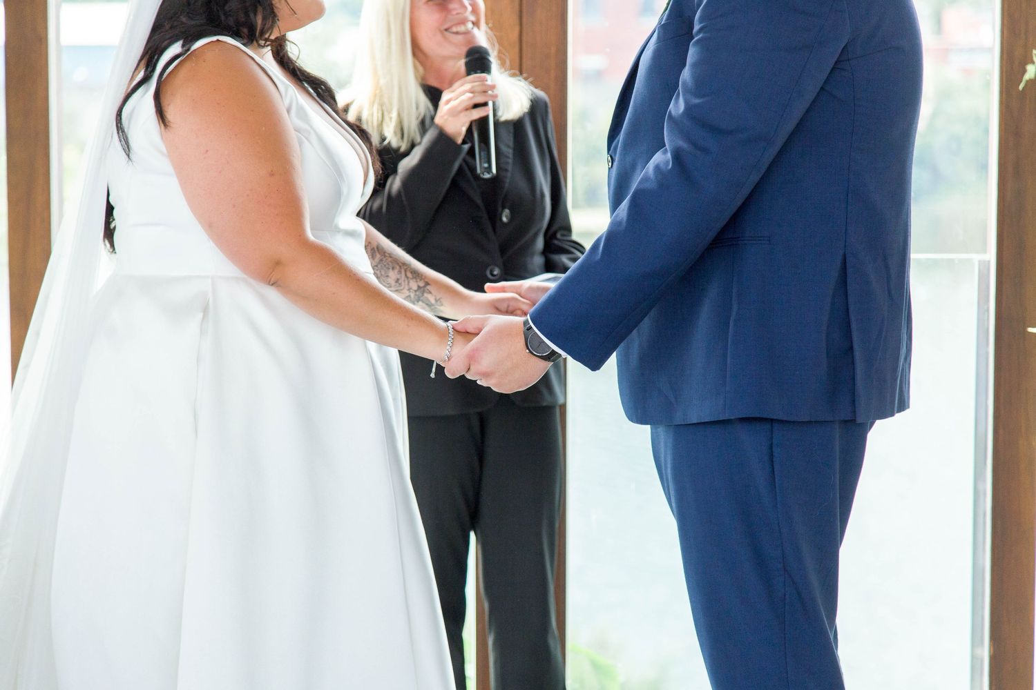 A bride and groom hold hands during their wedding ceremony while an officiant speaks behind them.