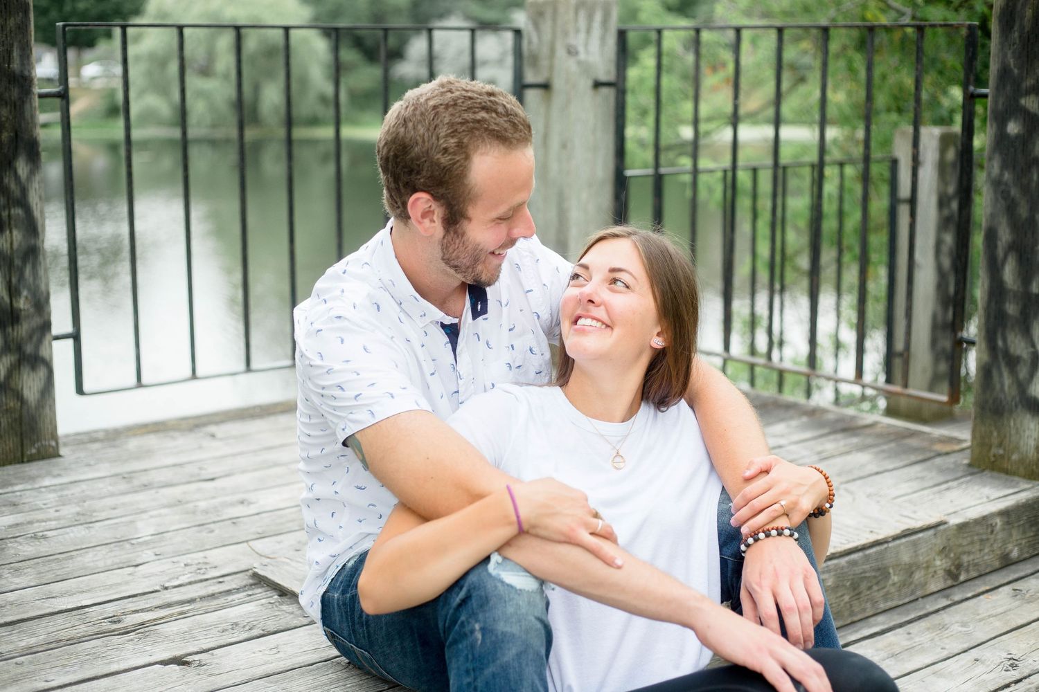 Couple sitting on wooden deck smiling at each other near a river.