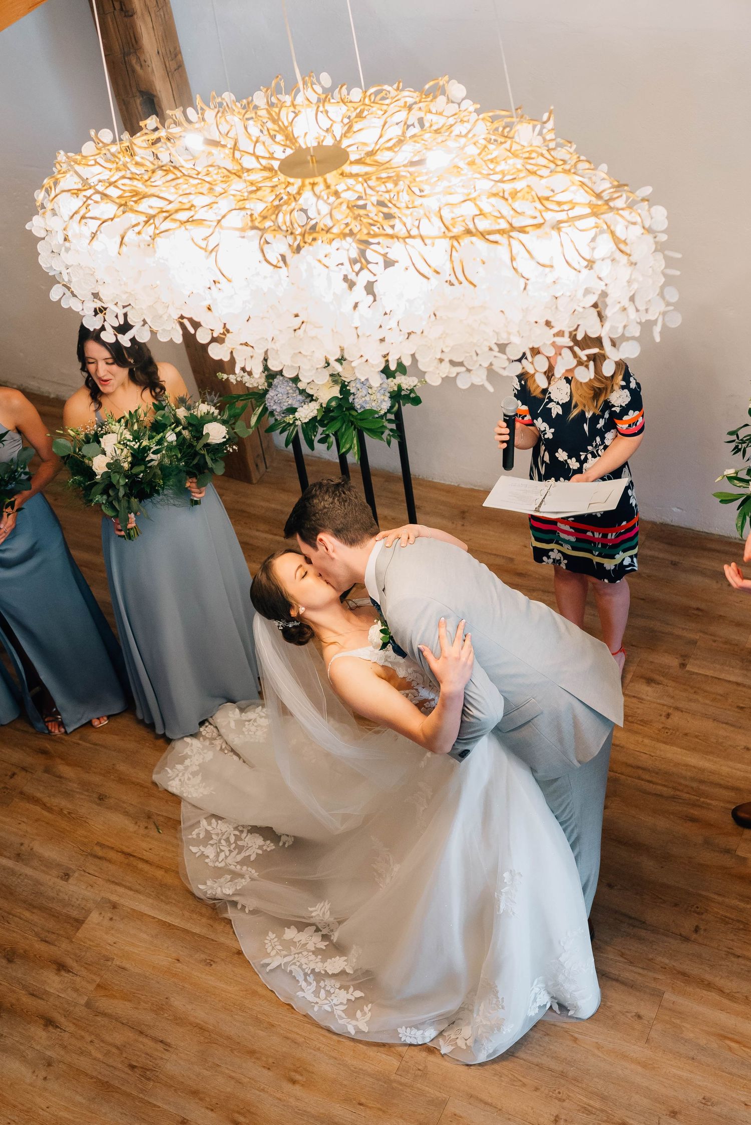 Bride and groom sharing first kiss under elegant floral chandelier at wedding ceremony.