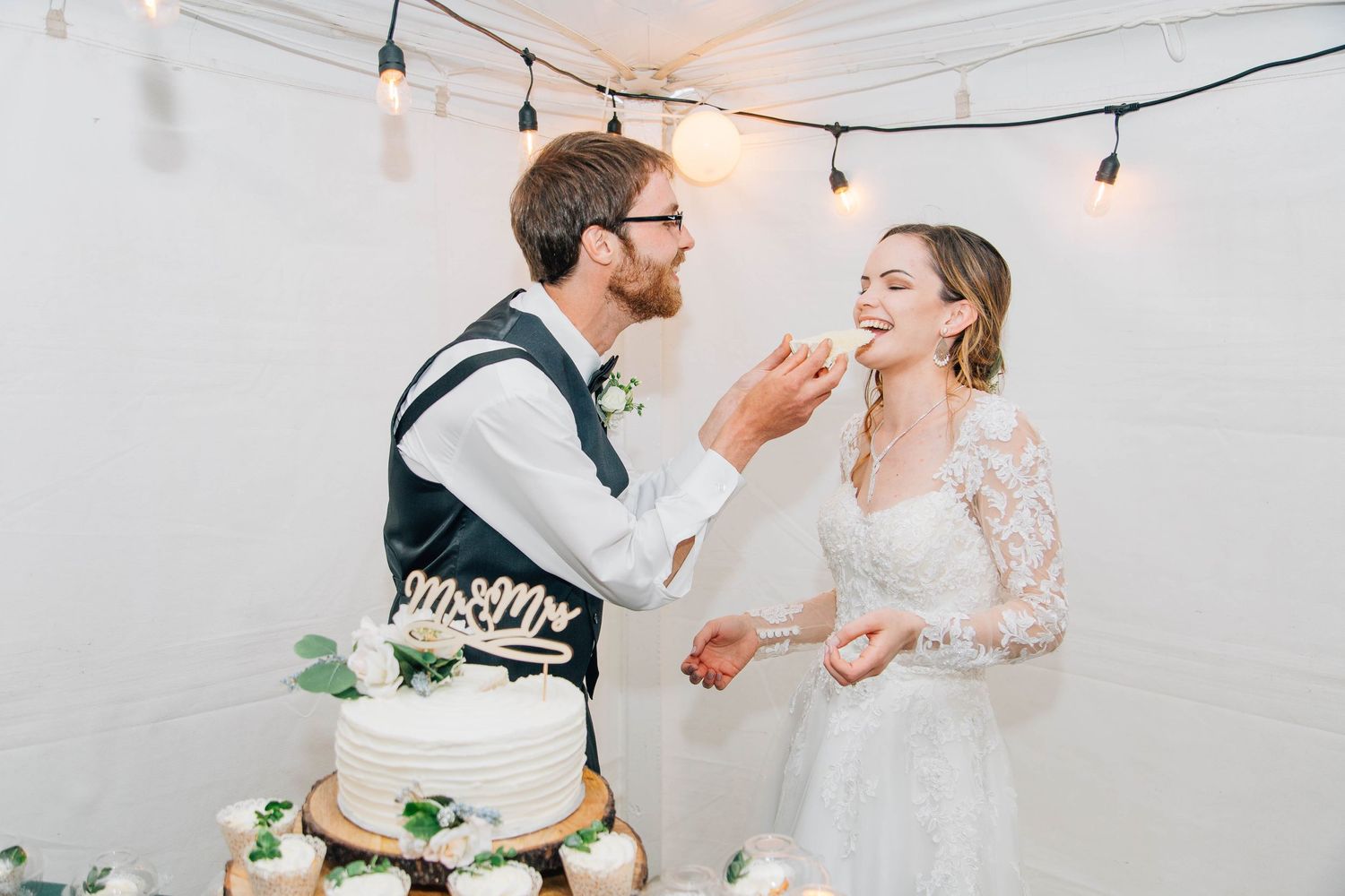 Groom feeding bride a bite of wedding cake at elegant indoor reception celebration.