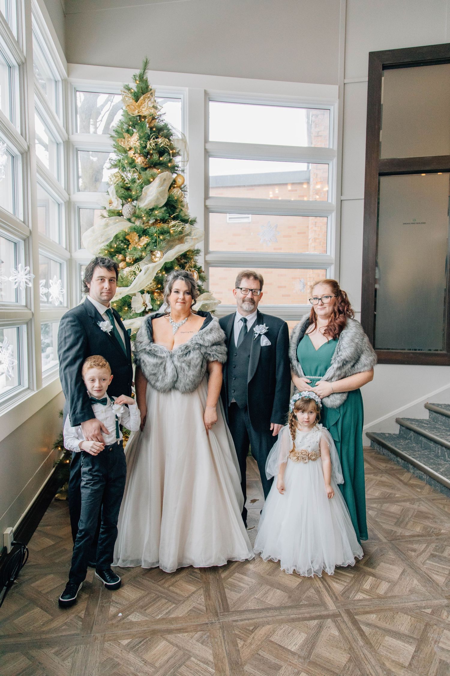 Wedding couple with family including children pose beside a decorated Christmas tree indoors.