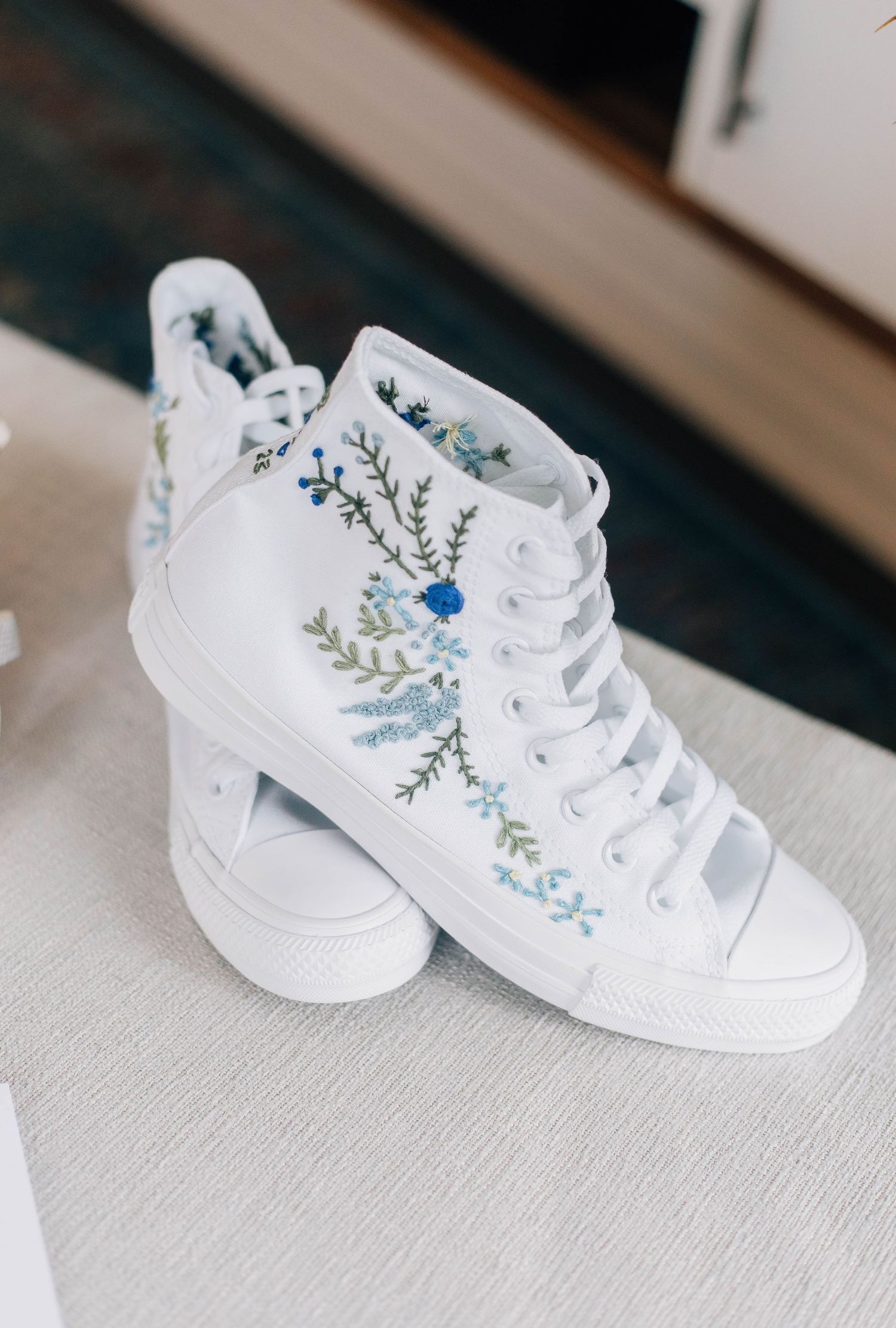 White high-top sneakers with blue floral embroidery displayed as bridal wedding shoes.