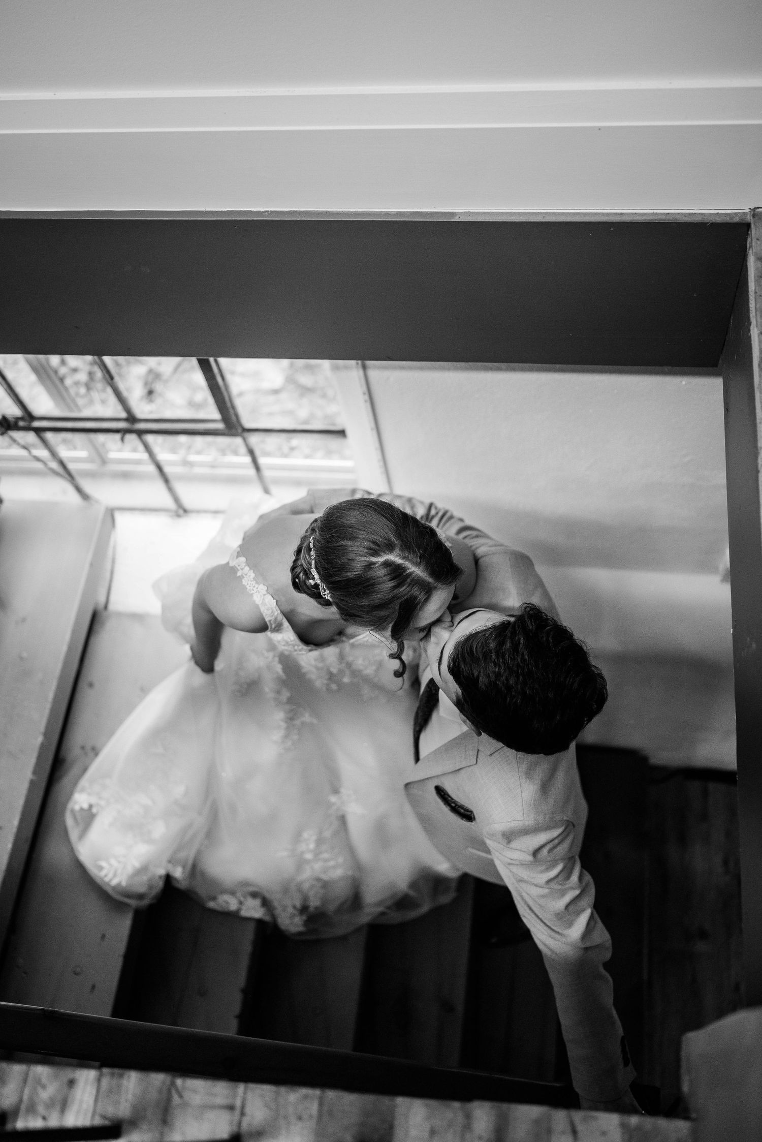 Aerial black and white photo of bride in white gown embracing groom on wedding venue staircase.