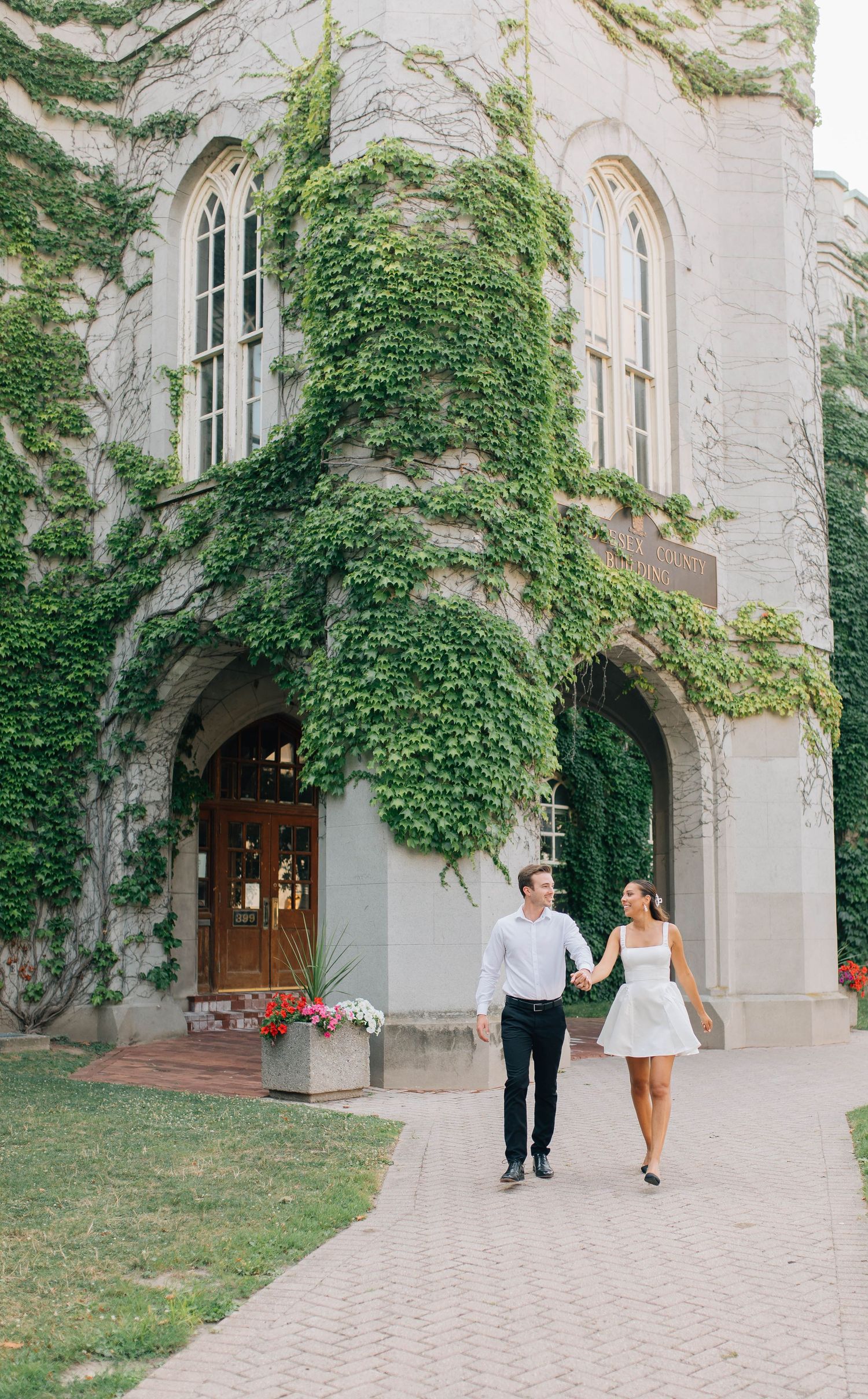 Wide shot of couple walking in front of the Old Courthouse in London Ontario
