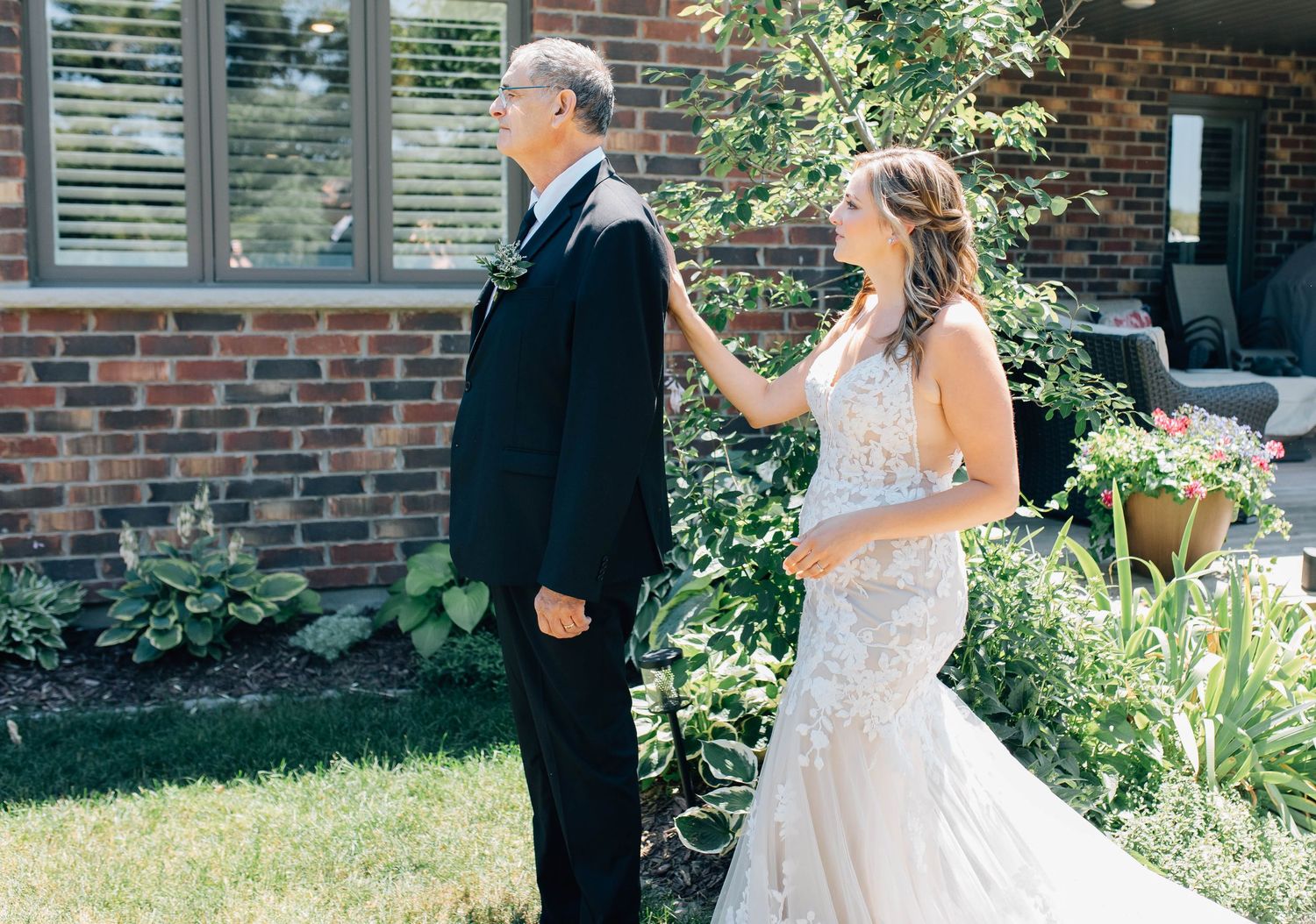 Bride in a lace gown taps her fathers shoulder during an emotional first look outside the family home in New Hamburg.