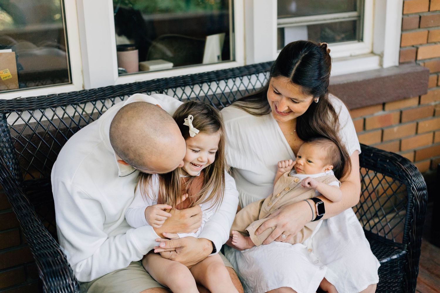 Happy family of four sitting on a porch bench with a toddler and newborn baby.