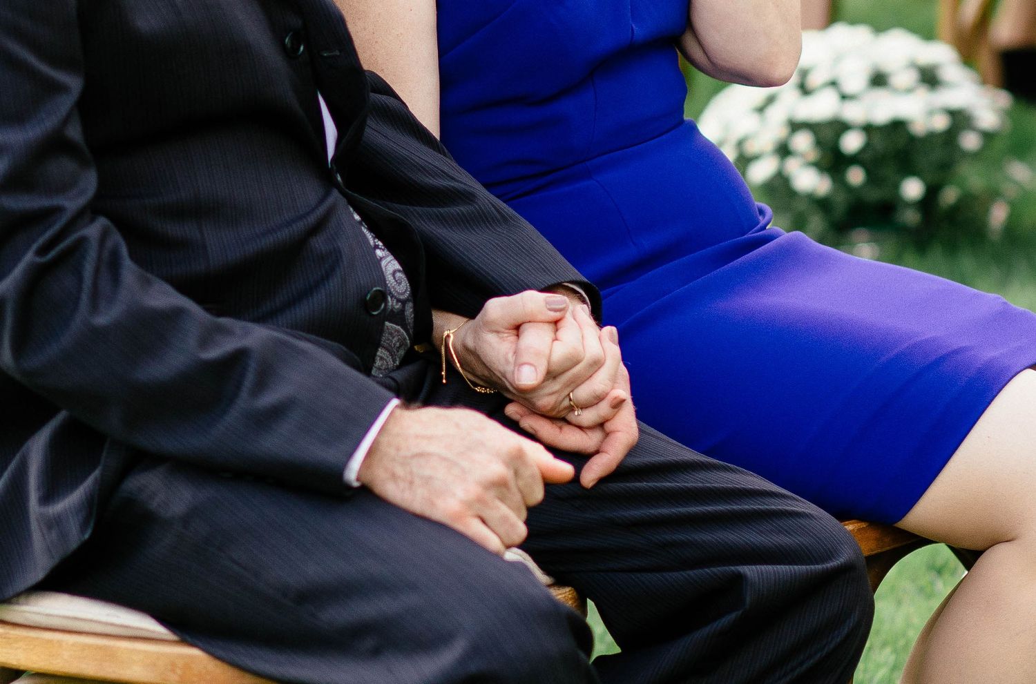 Couple holds hands tenderly during a wedding ceremony, woman wearing a royal blue dress.