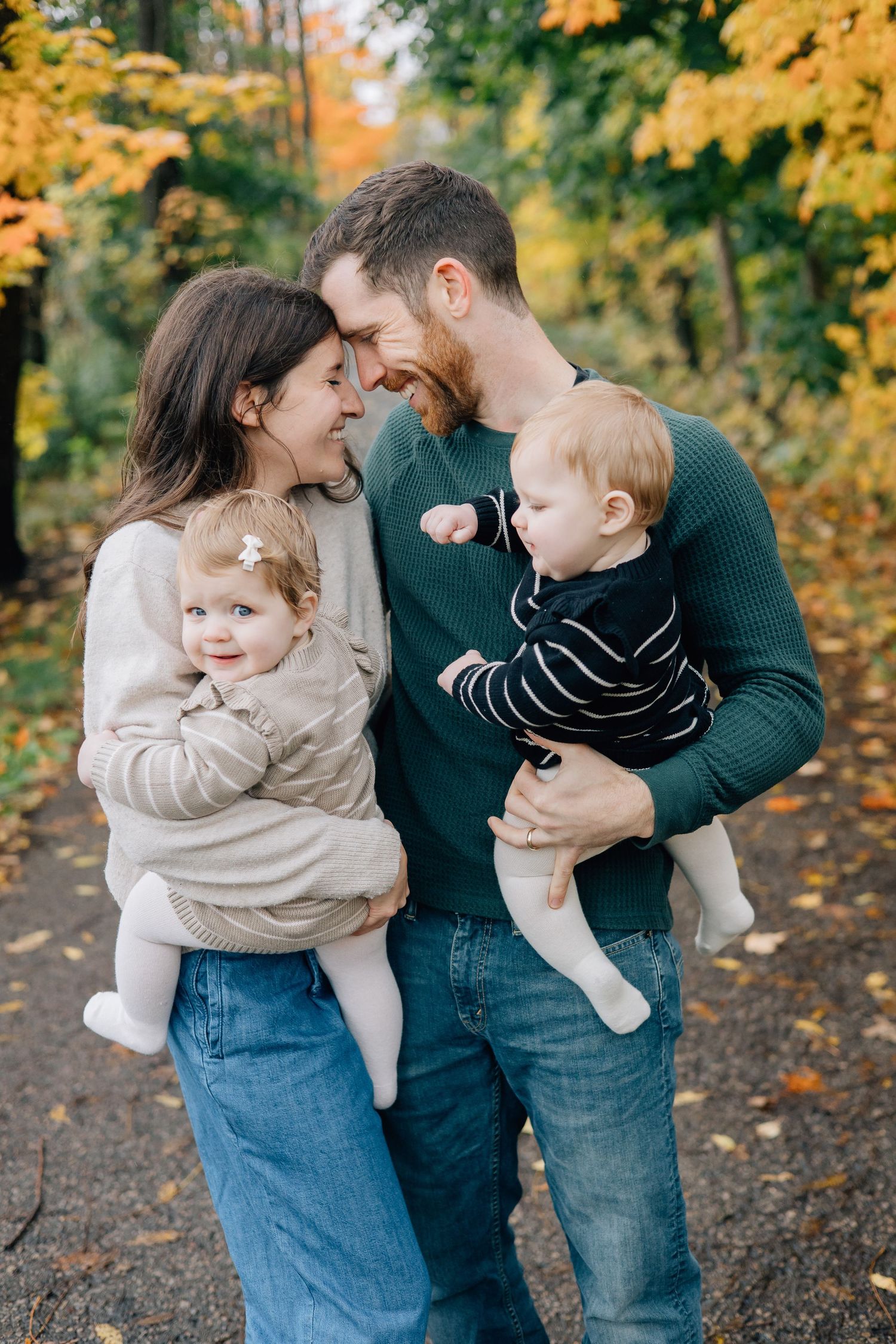 Loving couple with two babies touching foreheads in colorful autumn forest setting.