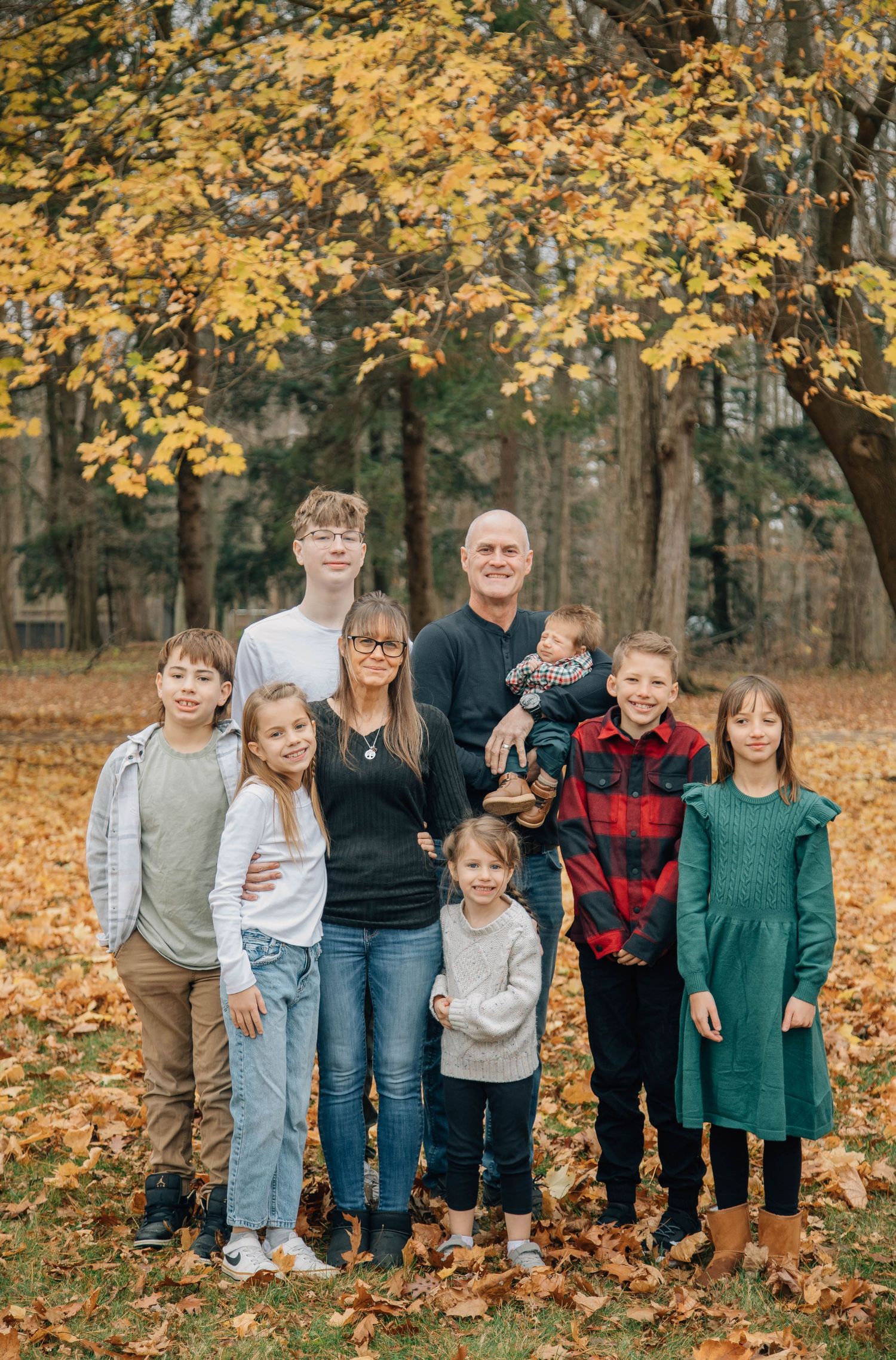 Large multigenerational family posing together under a golden autumn tree in a park.