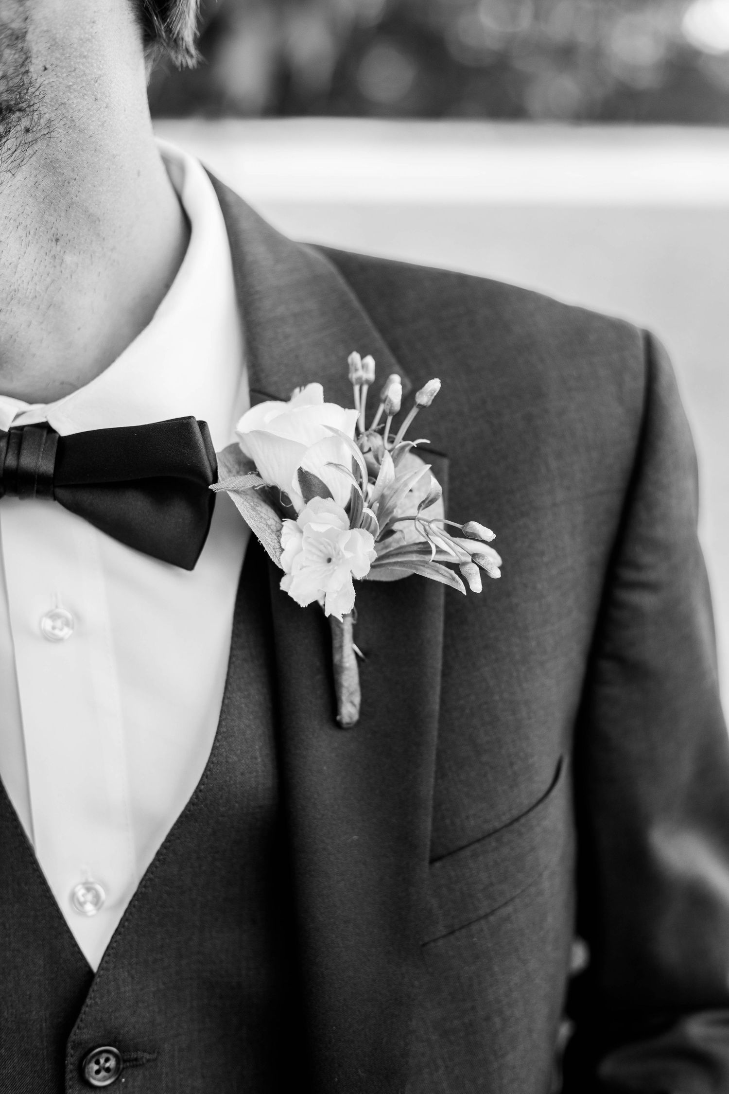 Black and white photo of a groom in a suit with bow tie and floral boutonniere on his lapel.