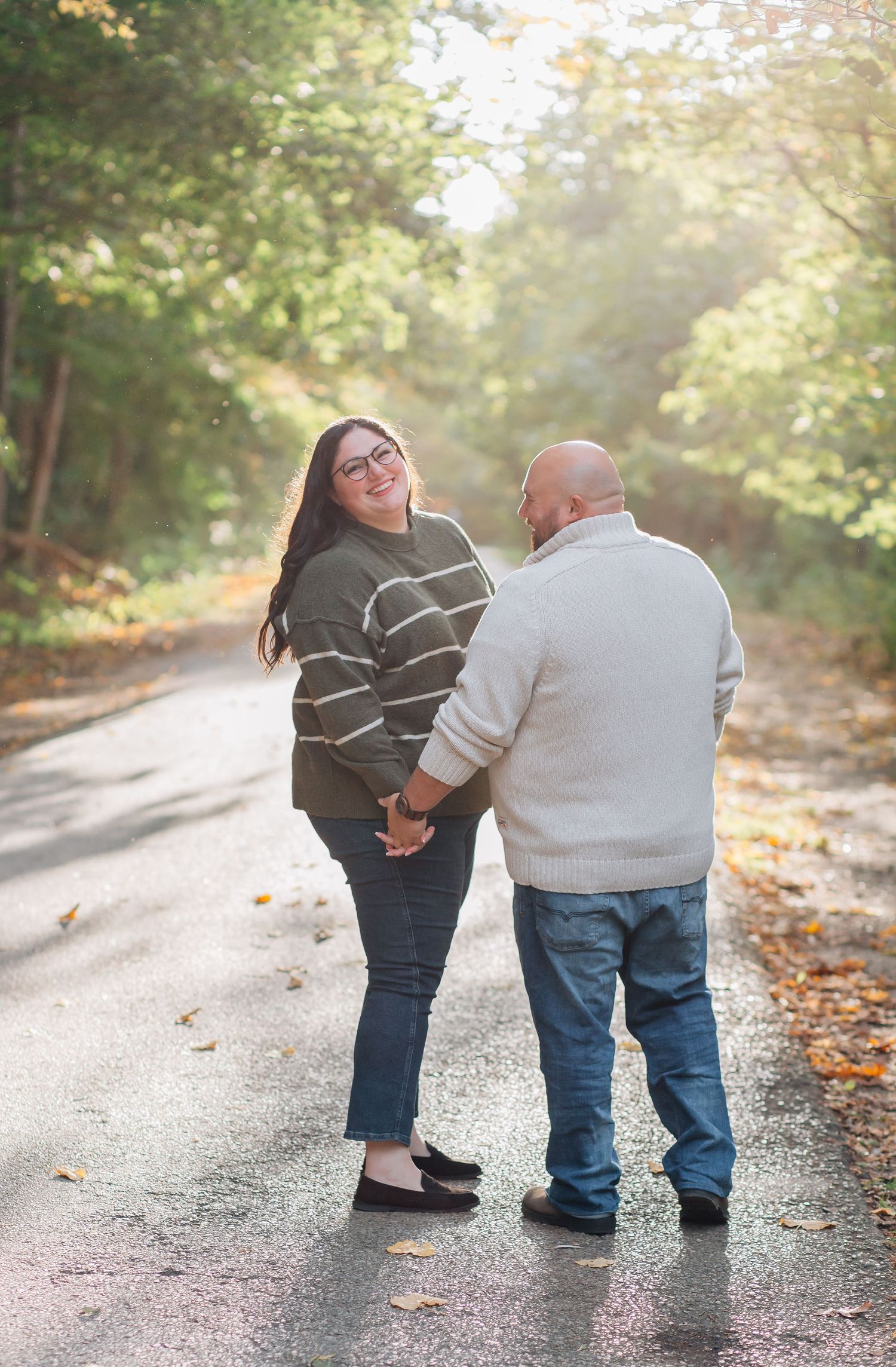 Couple holding hands on a sunlit autumn road surrounded by golden-leaved trees.
