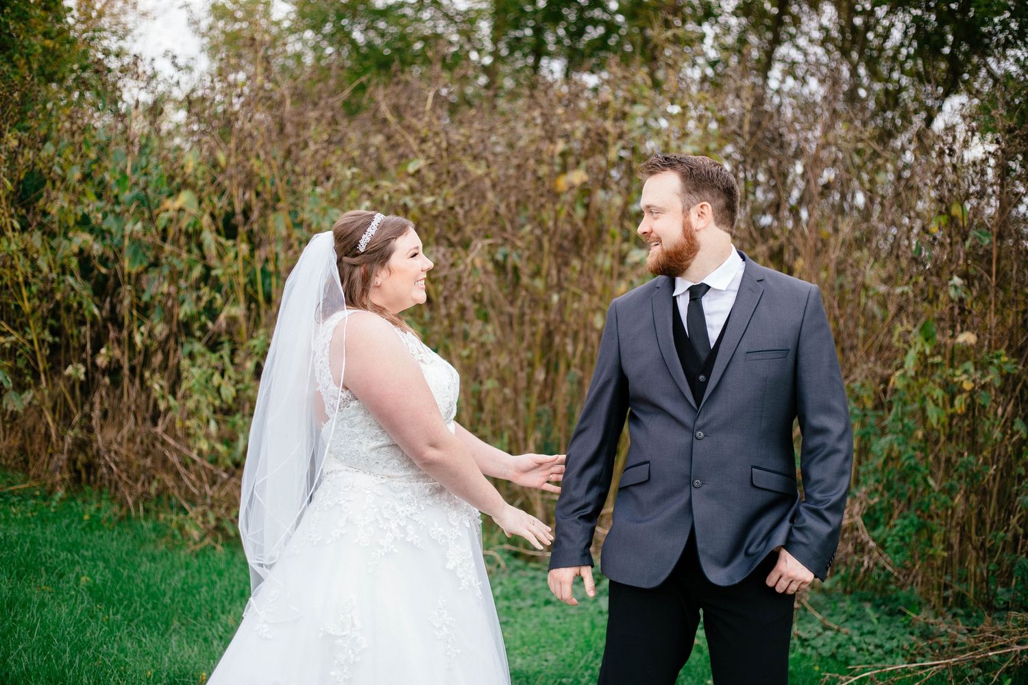 Bride and groom holding hands sharing a smile during outdoor first look at wedding.