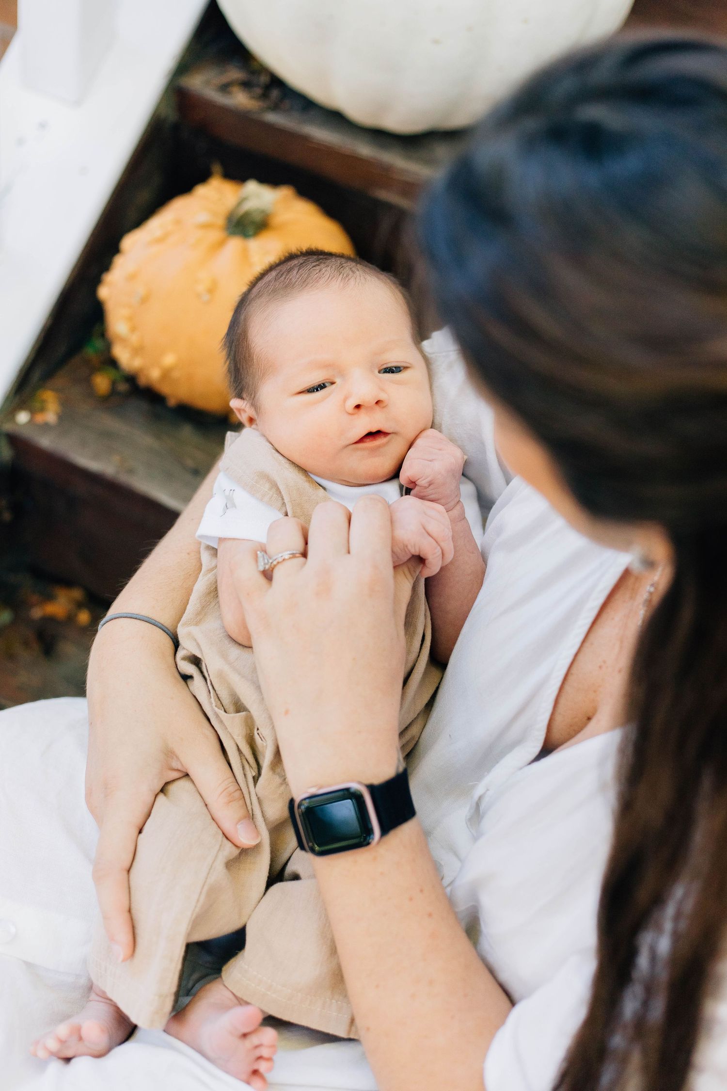 Close-up overhead view of alert newborn baby in tan outfit being held by mother wearing an Apple Watch.