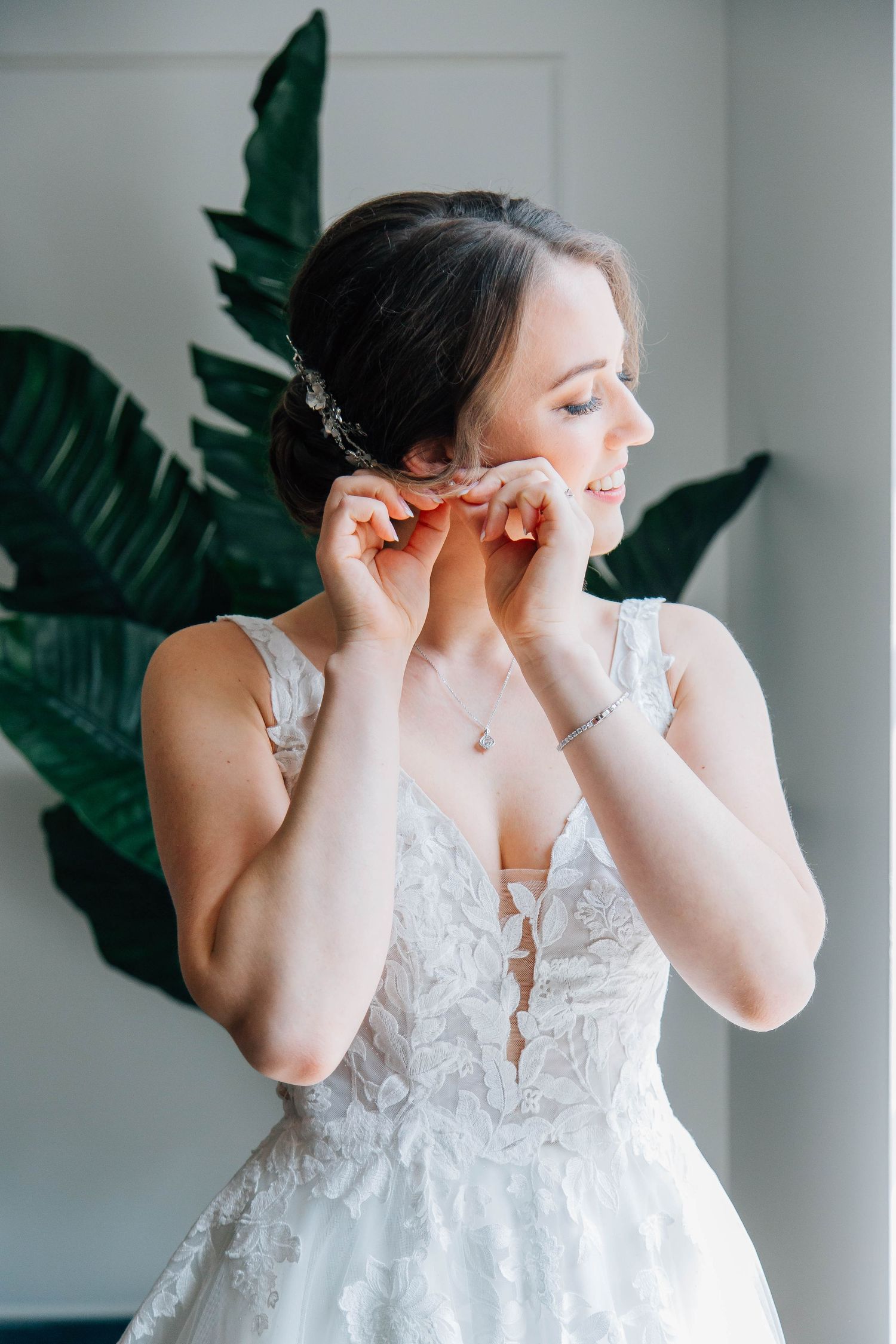 Elegant bride in lace wedding gown adjusts her earring while getting ready for the ceremony.