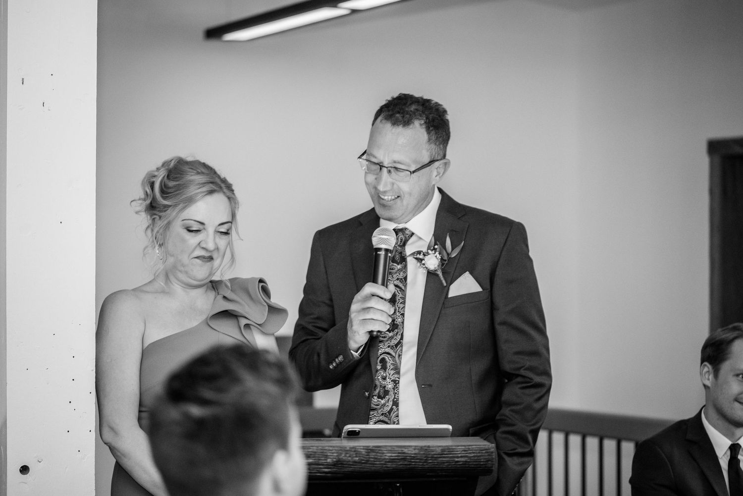Man and woman sharing microphone at wedding podium giving a speech in black and white photo.