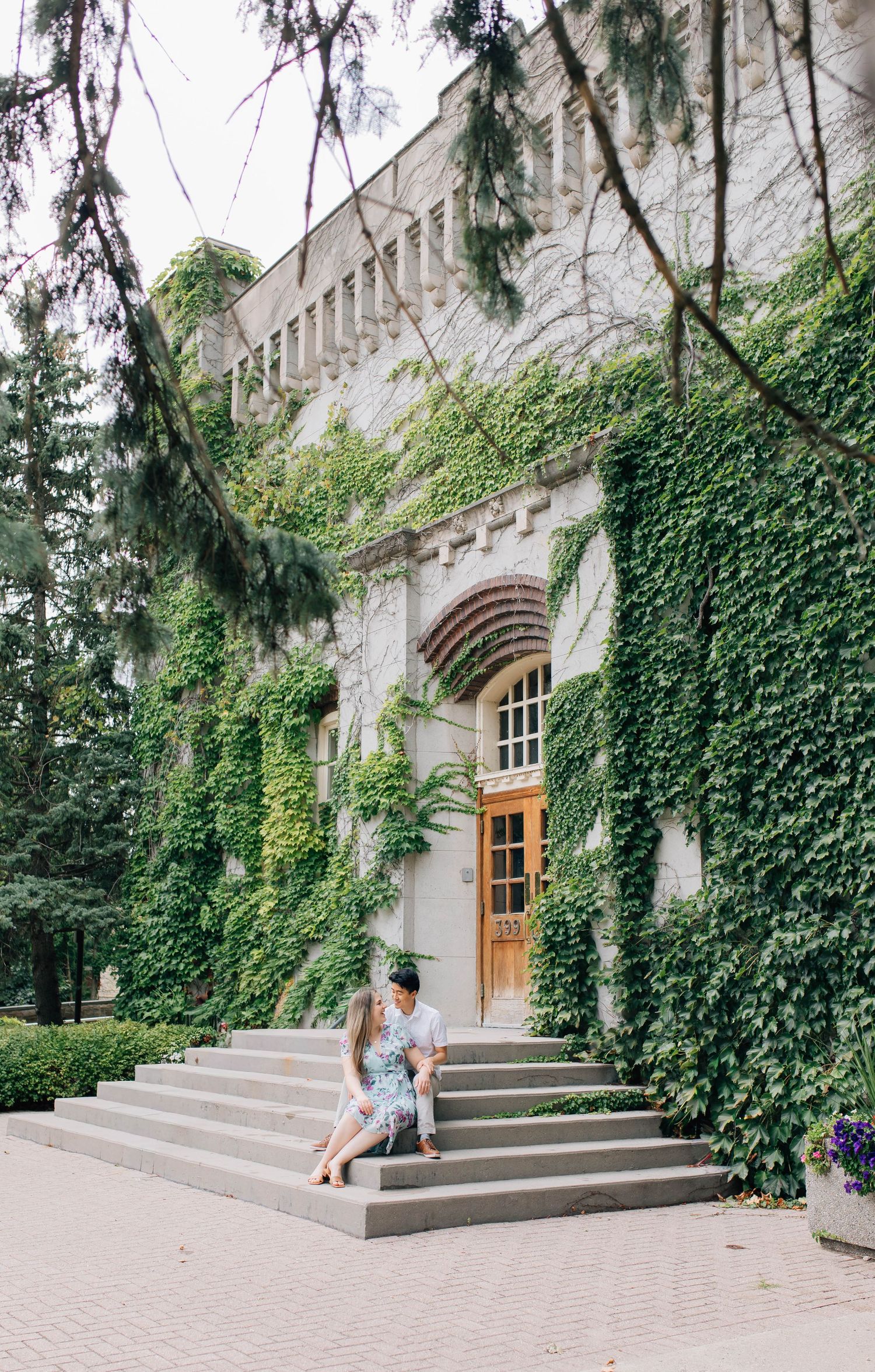 Couple sitting on steps of ivy-covered stone building, sharing an intimate moment at historic venue.