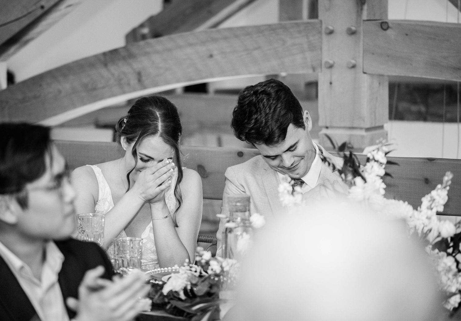 Emotional bride and groom reacting to heartfelt wedding speeches at decorated reception table.