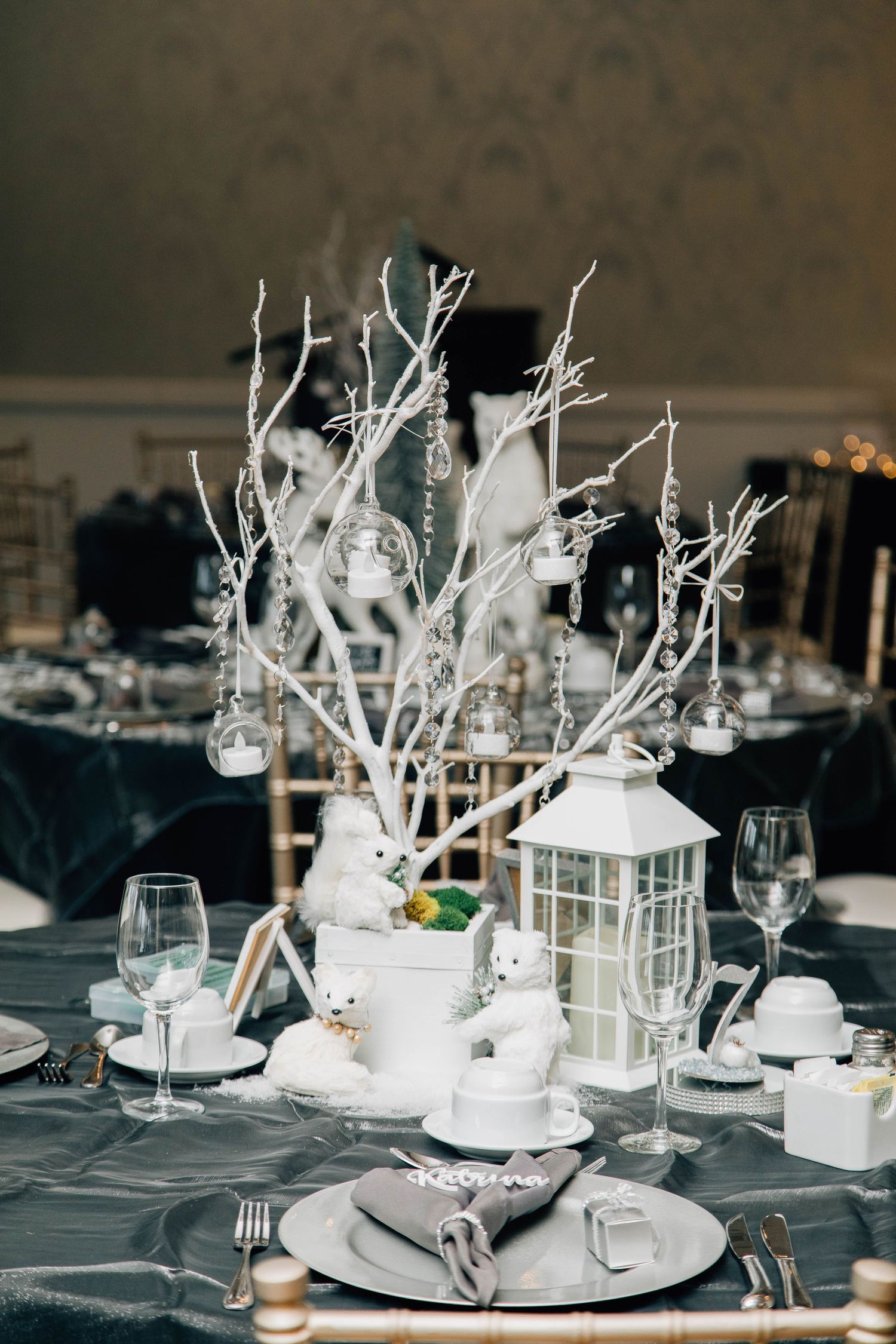 Winter wedding centerpiece with white bare branches, hanging crystals, polar bear figurines, and a white lantern.