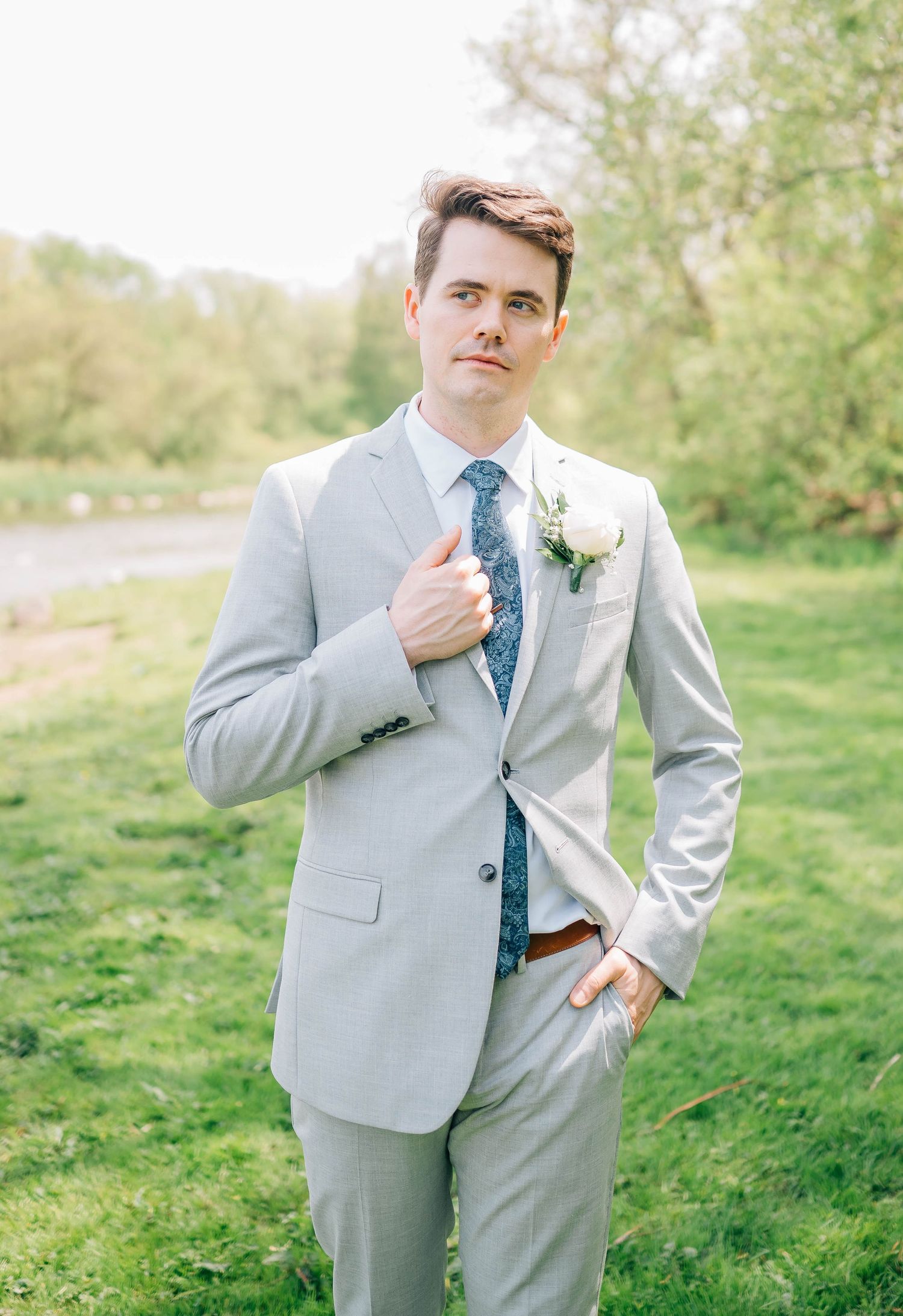 Groom in light gray suit and blue floral tie poses outdoors on wedding day.