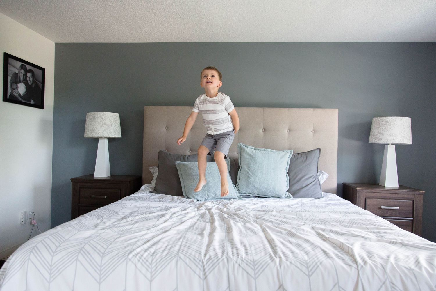 Energetic young boy jumping on a large bed in a modern bedroom.