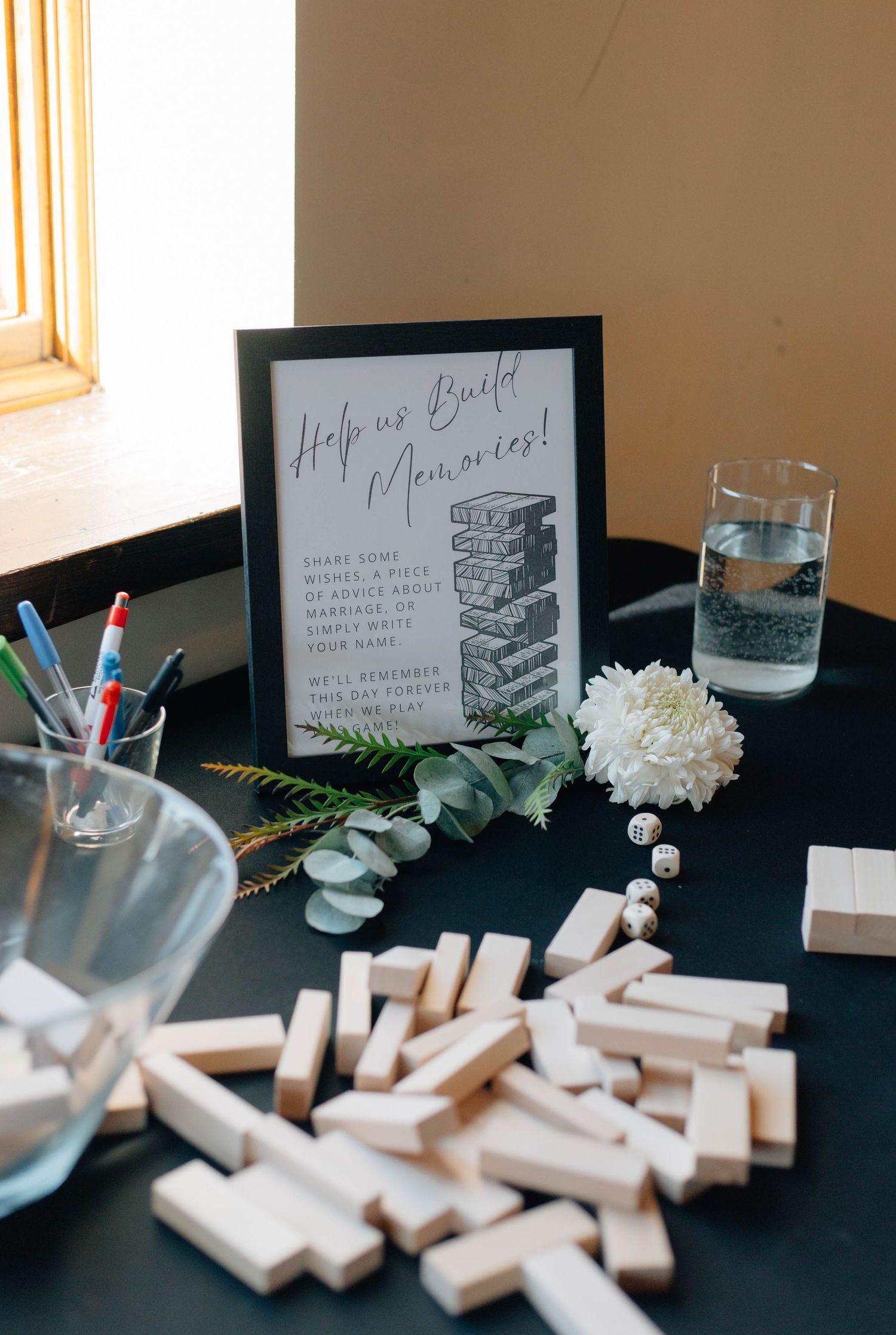 Wedding guest book station featuring Jenga blocks and a Help Us Build Memories sign with florals.