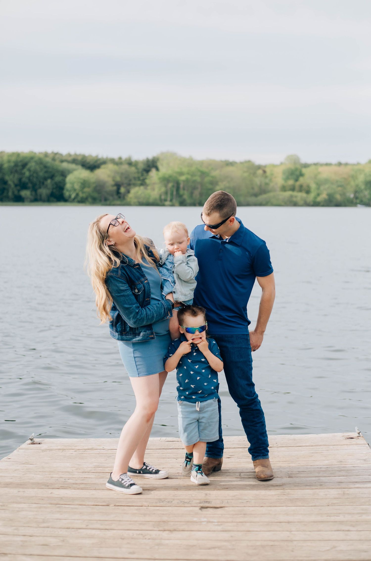 Young family with two small children posing on a wooden dock beside a calm lake.