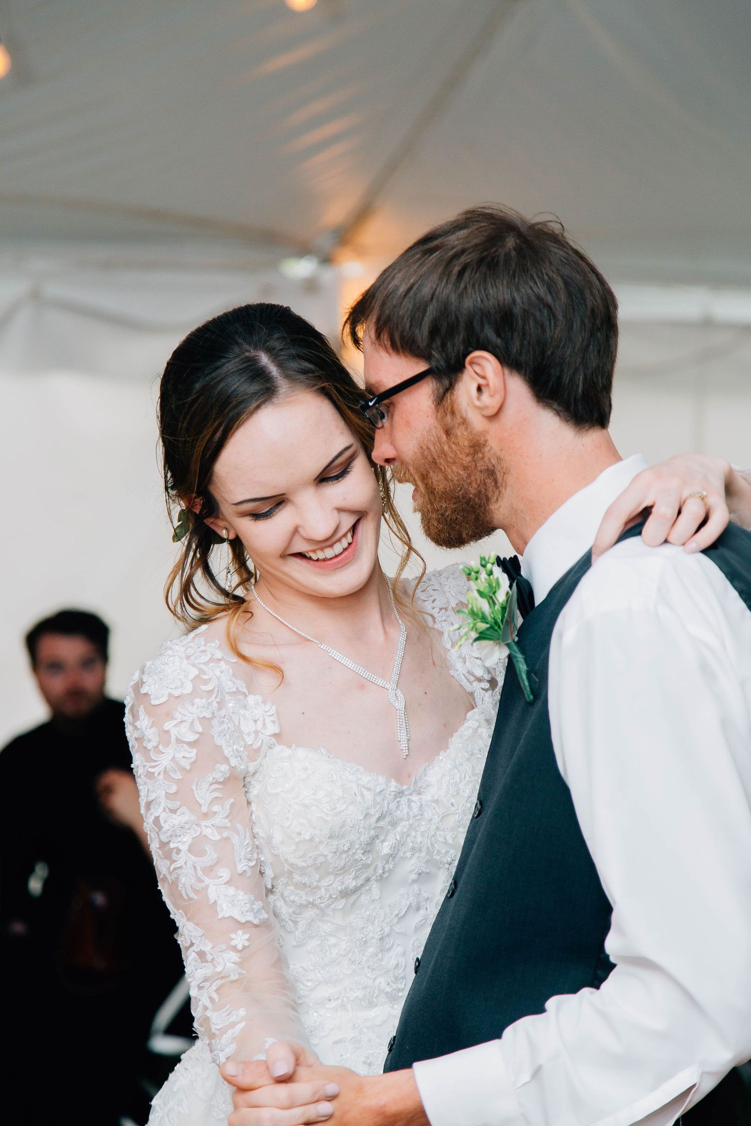 Joyful bride laughs as groom whispers to her during their intimate first dance at reception.
