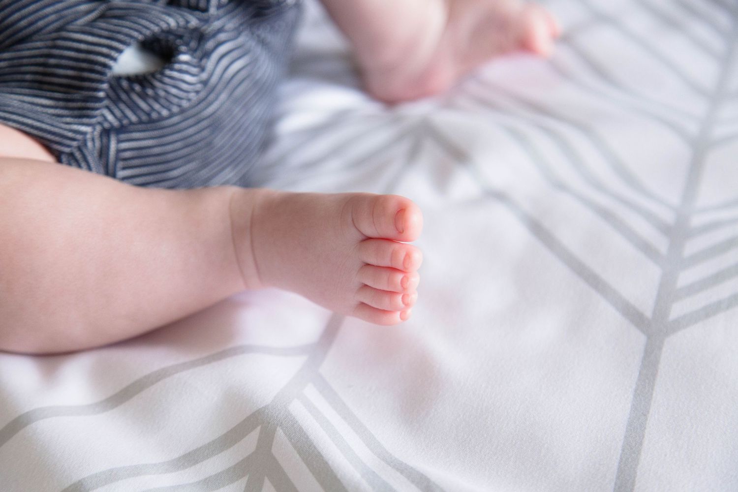 Close-up of tiny newborn baby feet resting on a white patterned blanket.
