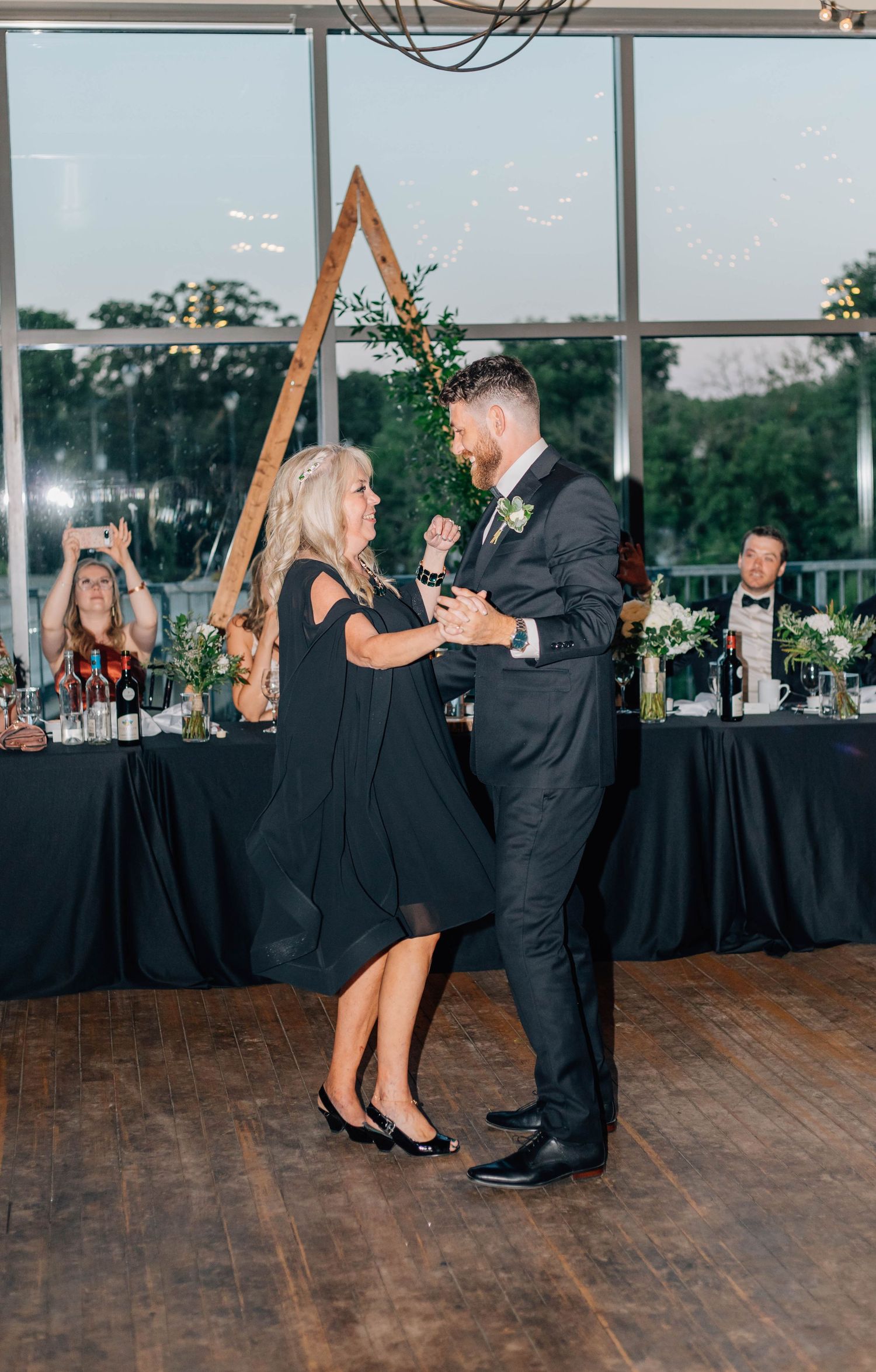 Groom shares special mother-son dance with mom in black dress at elegant wedding reception venue.