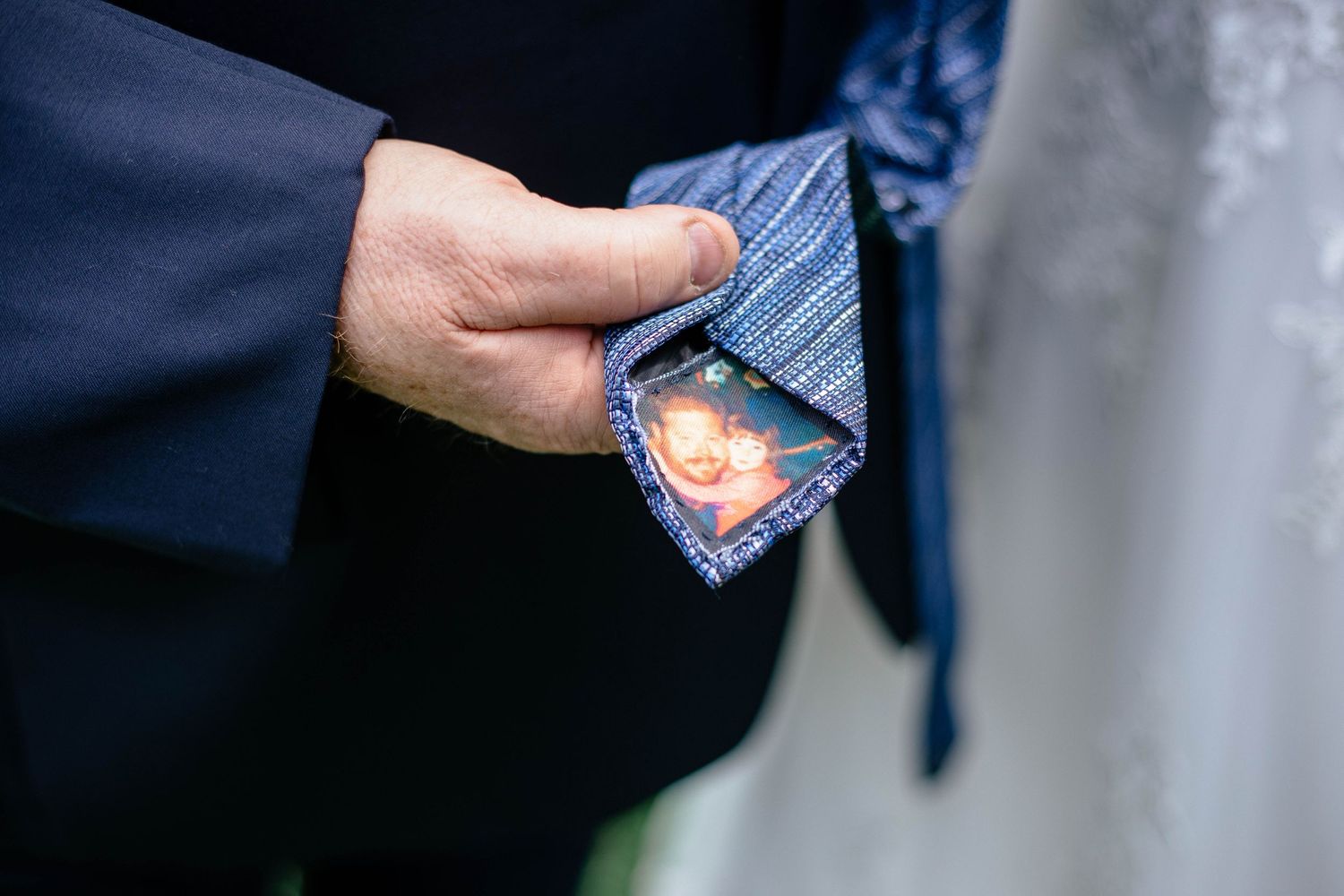 Groom revealing hidden photo inside blue tie lining as sentimental wedding day surprise.