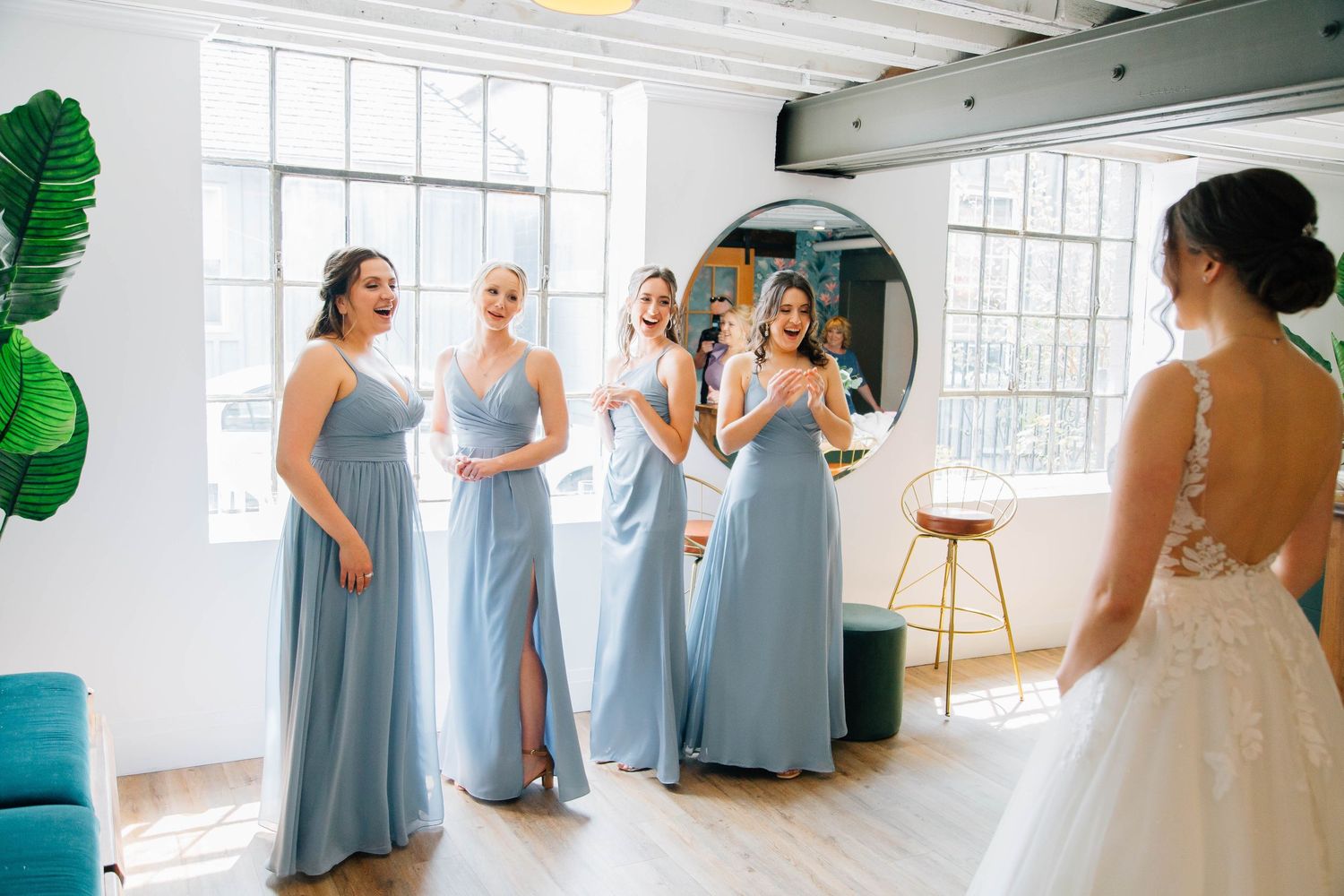 Bridesmaids in light blue gowns react with excitement as bride reveals her wedding dress.