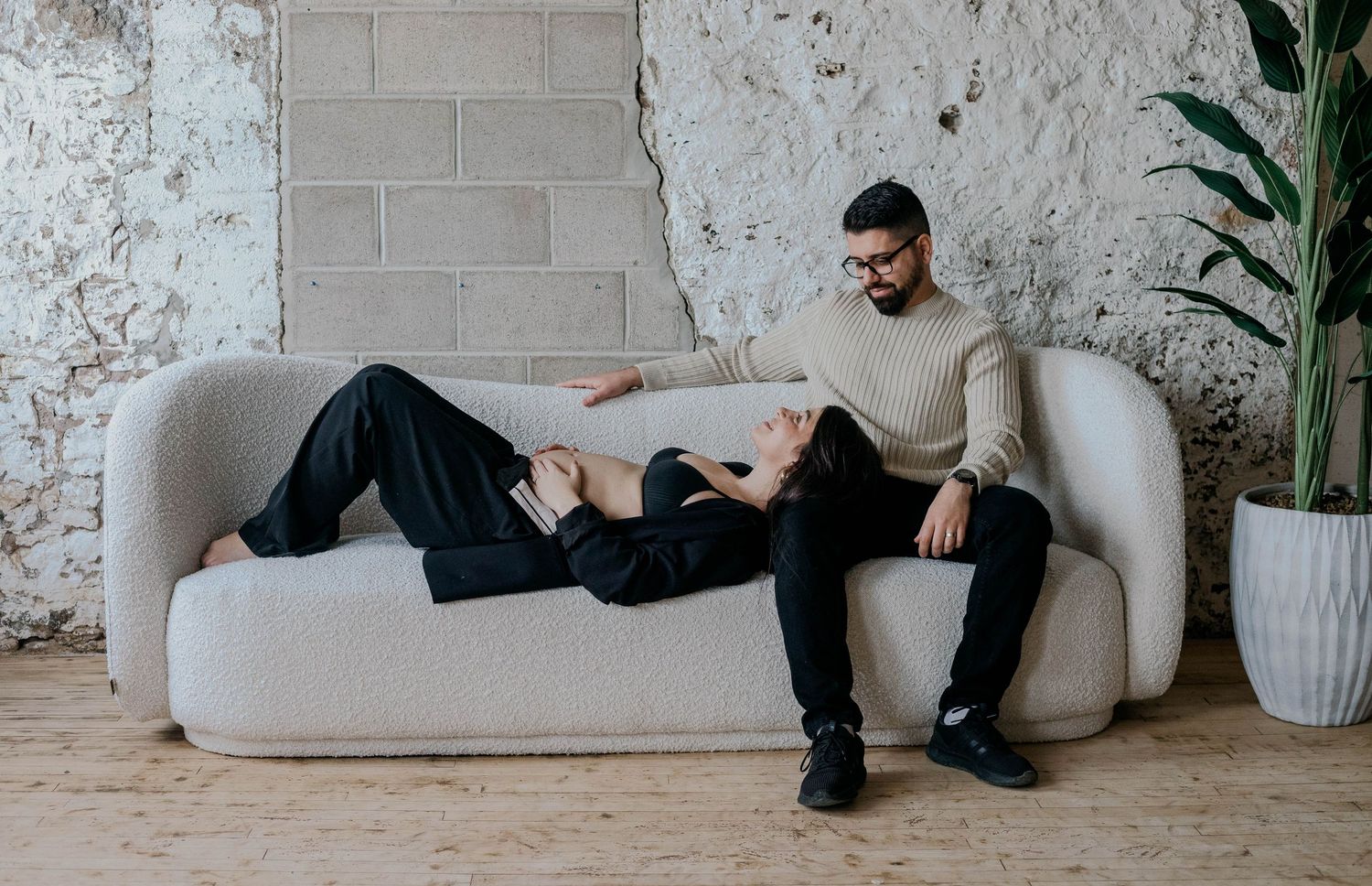 Expecting couple relaxing on modern sofa during casual indoor maternity photoshoot.