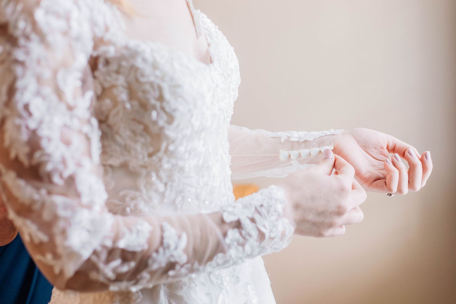 Close-up of bride in lace long-sleeve wedding dress adjusting her delicate button cuff.