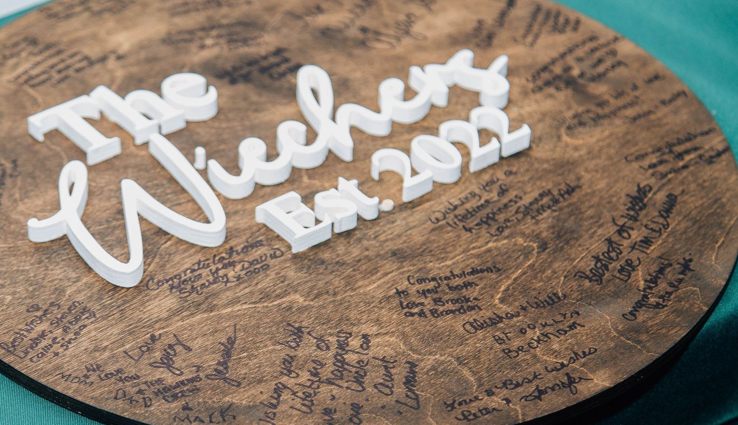 Wooden wedding guest book sign reading The Wiechers Est. 2022 with signatures.
