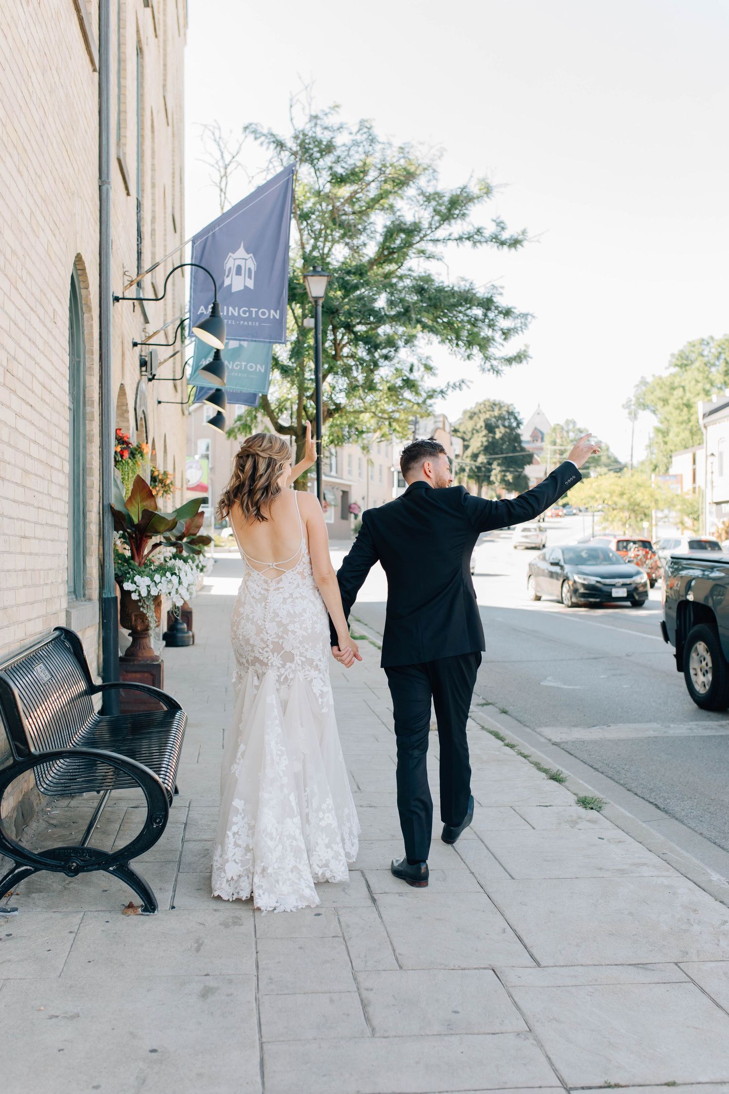 Wedding couple walks hand-in-hand past Arlington banner on charming downtown sidewalk on sunny day.