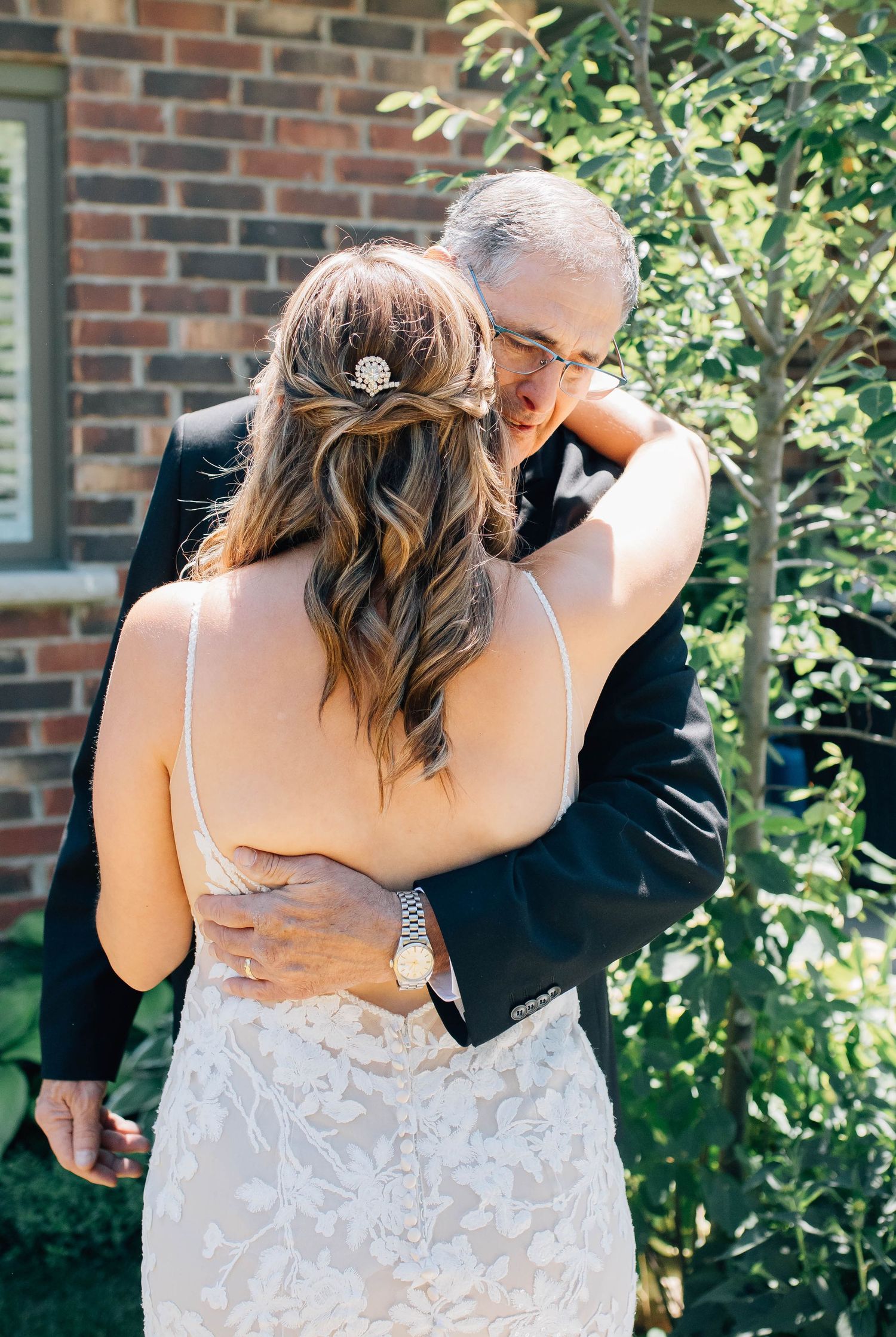 Father embraces his daughter in a lace wedding gown during an emotional first look at family home.