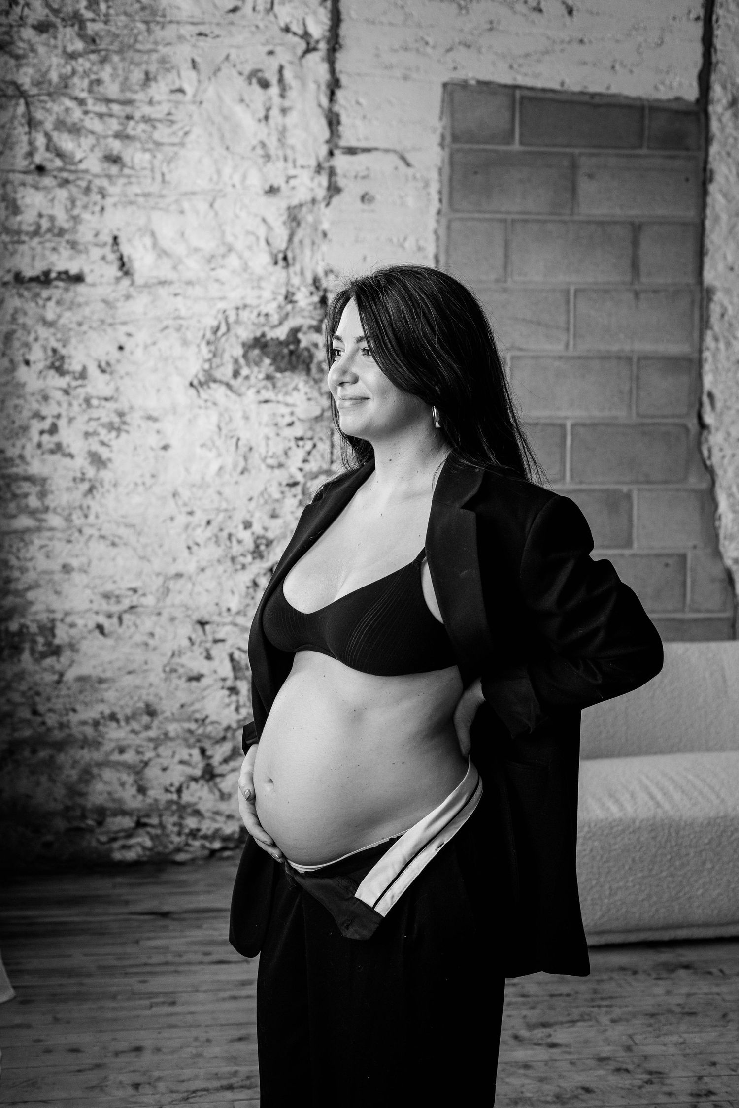 Black and white portrait of glowing pregnant woman in blazer cradling baby bump.