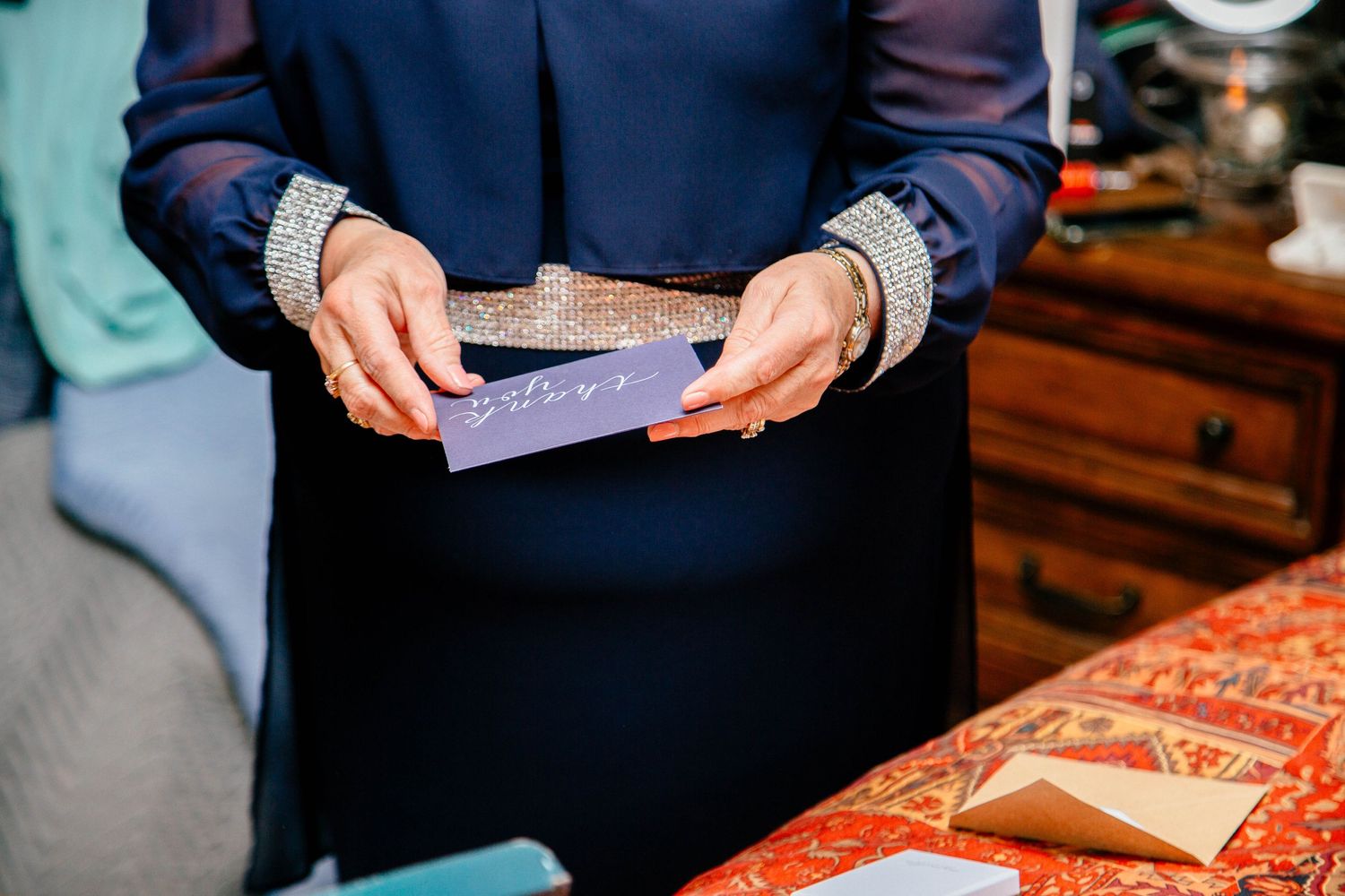 Woman in navy blue dress holding a purple wedding card with gold envelope on a decorative table.