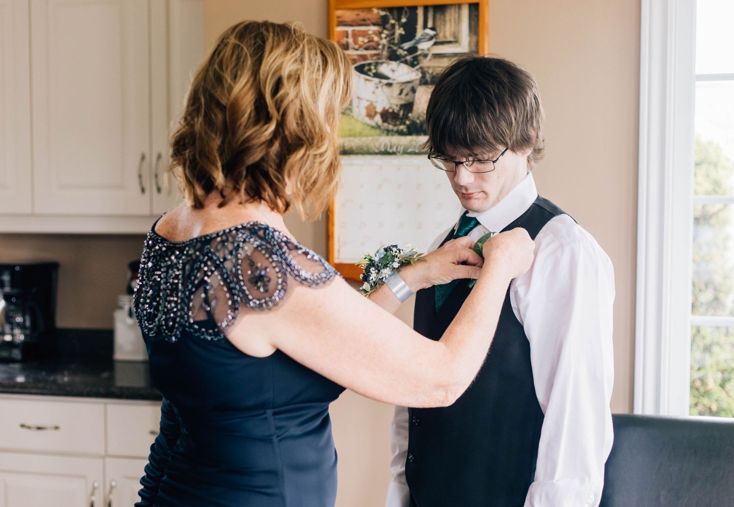 Mother in navy dress helping young man adjust his tie before a wedding ceremony.