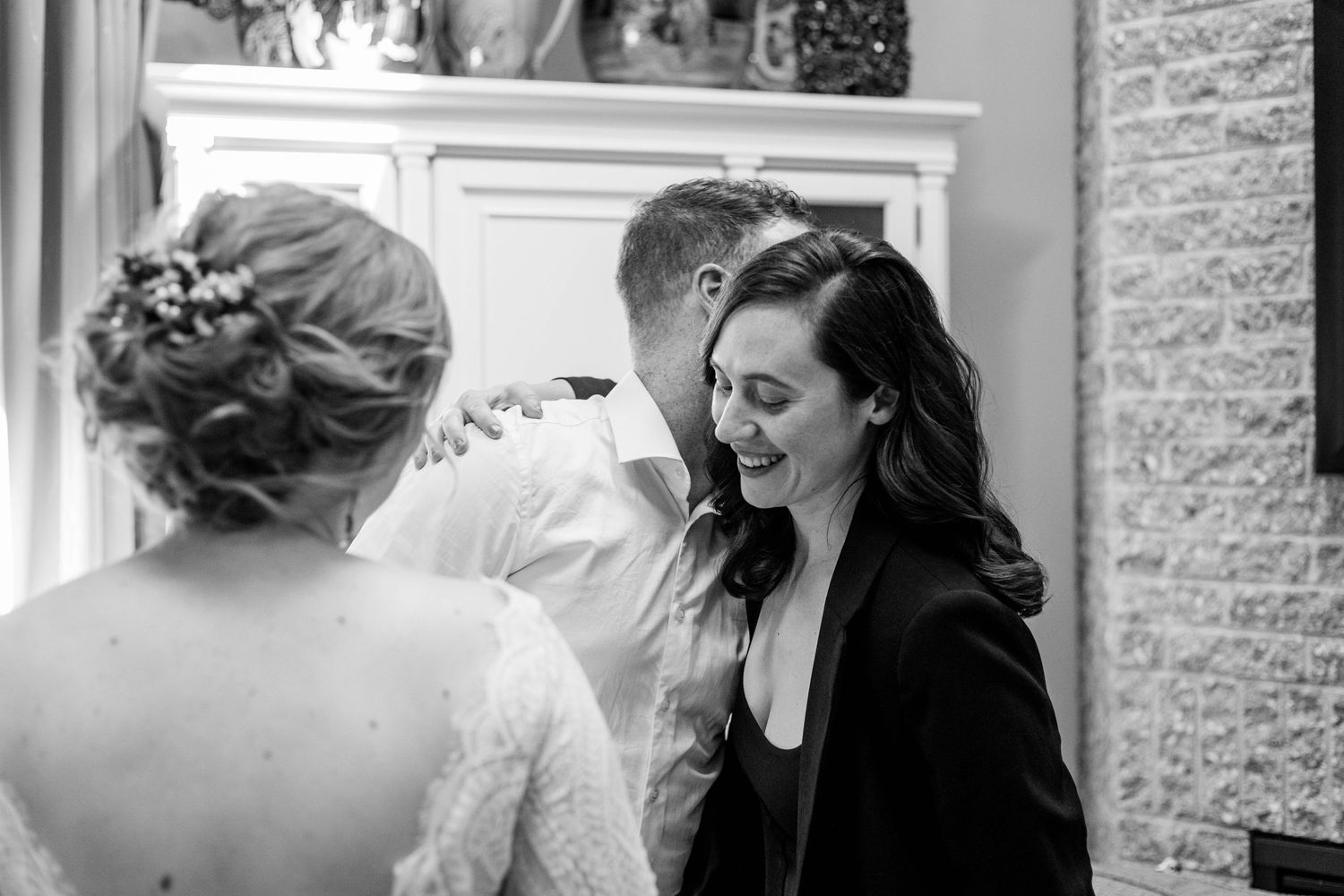 Black and white photo of a woman laughing with a bride and groom at a wedding.