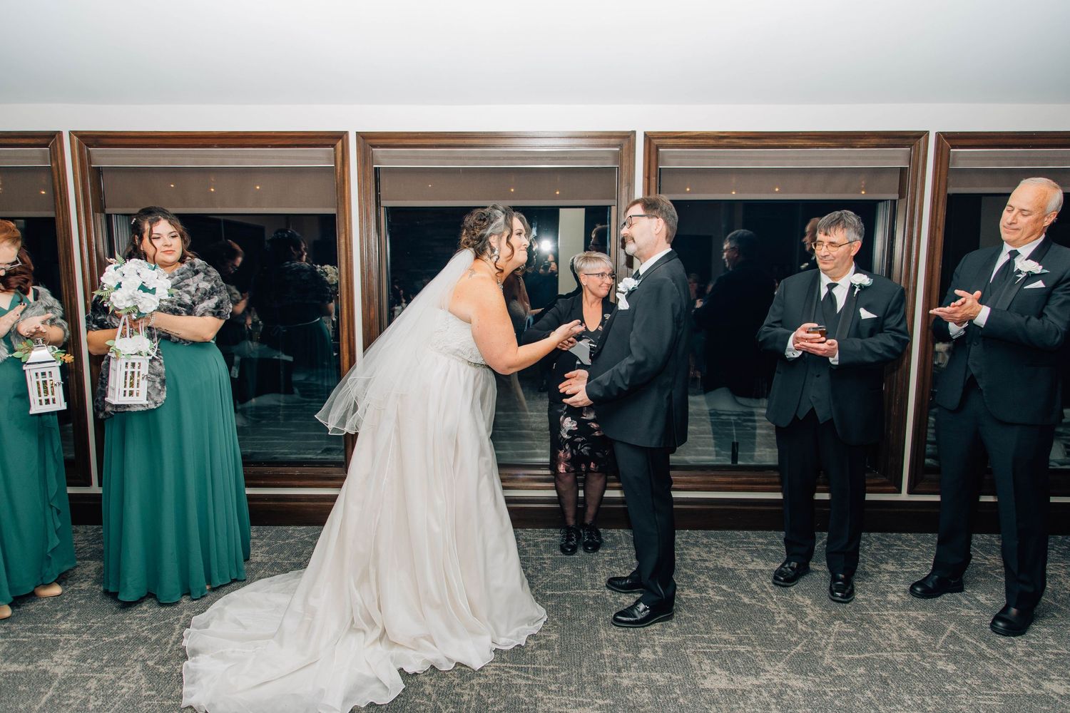 Bride and groom share first kiss at indoor wedding ceremony as guests in green dresses applaud.