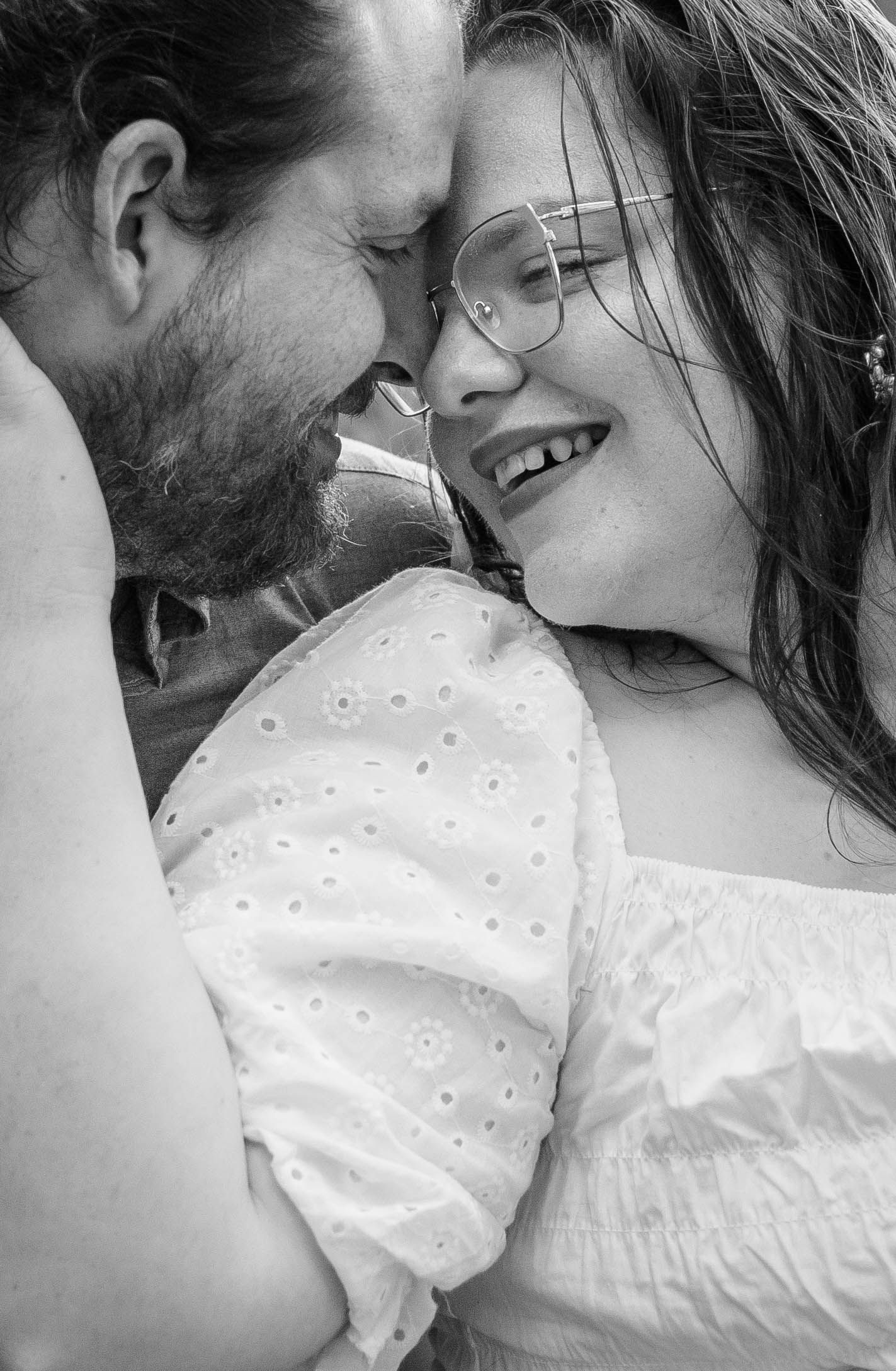 Black and white close-up of a smiling couple with glasses sharing a tender romantic moment.