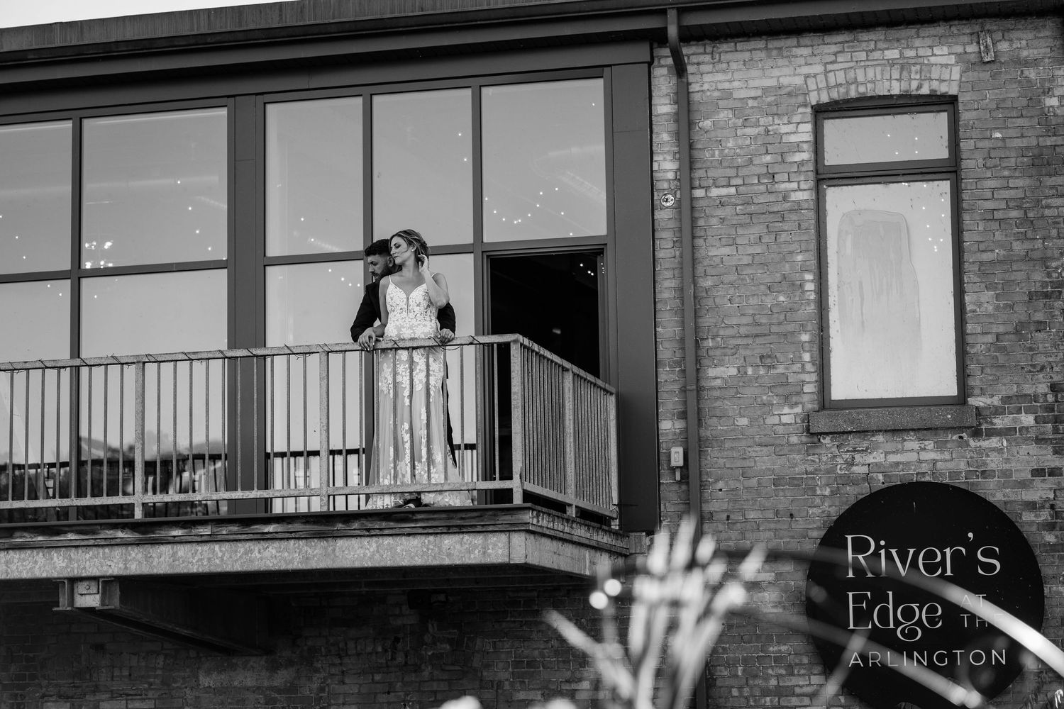 Black and white photo of bride on balcony at Rivers Edge Arlington wedding venue exterior.