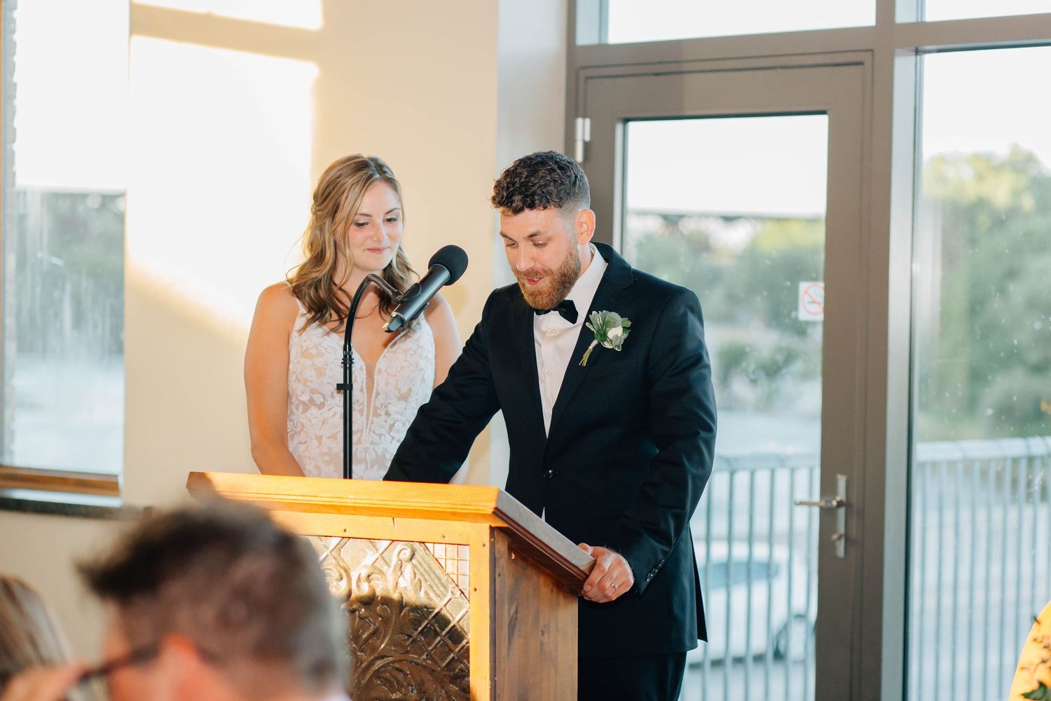 Bride and groom stand together at podium delivering heartfelt speech at their wedding reception.