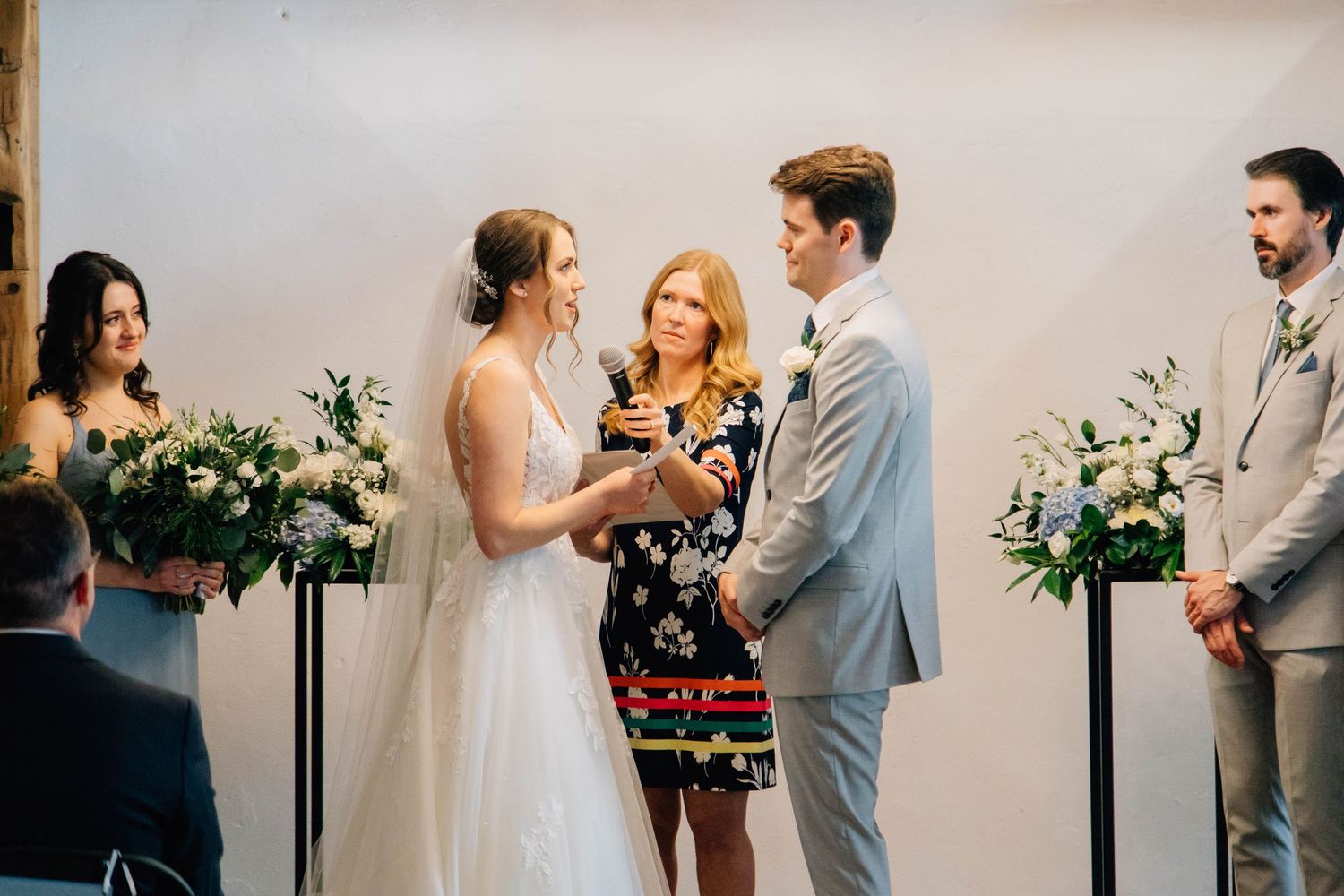 Couple exchanging vows during intimate indoor wedding ceremony with floral arrangements.