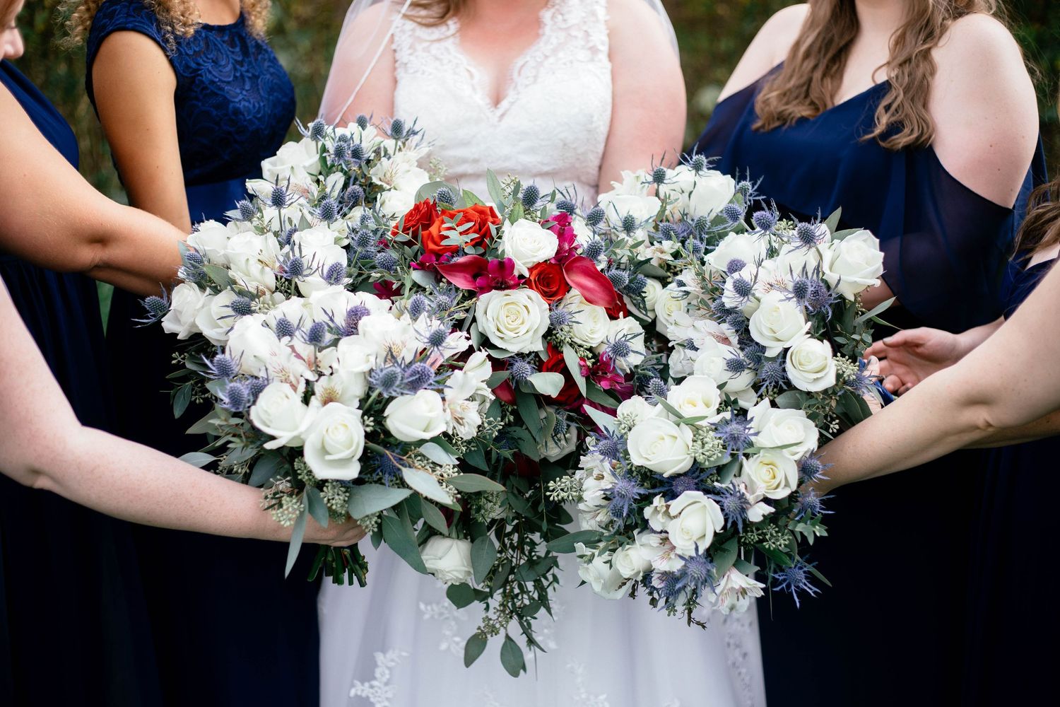 Close-up of bride and bridesmaids holding lush white, red, and blue floral wedding bouquets.
