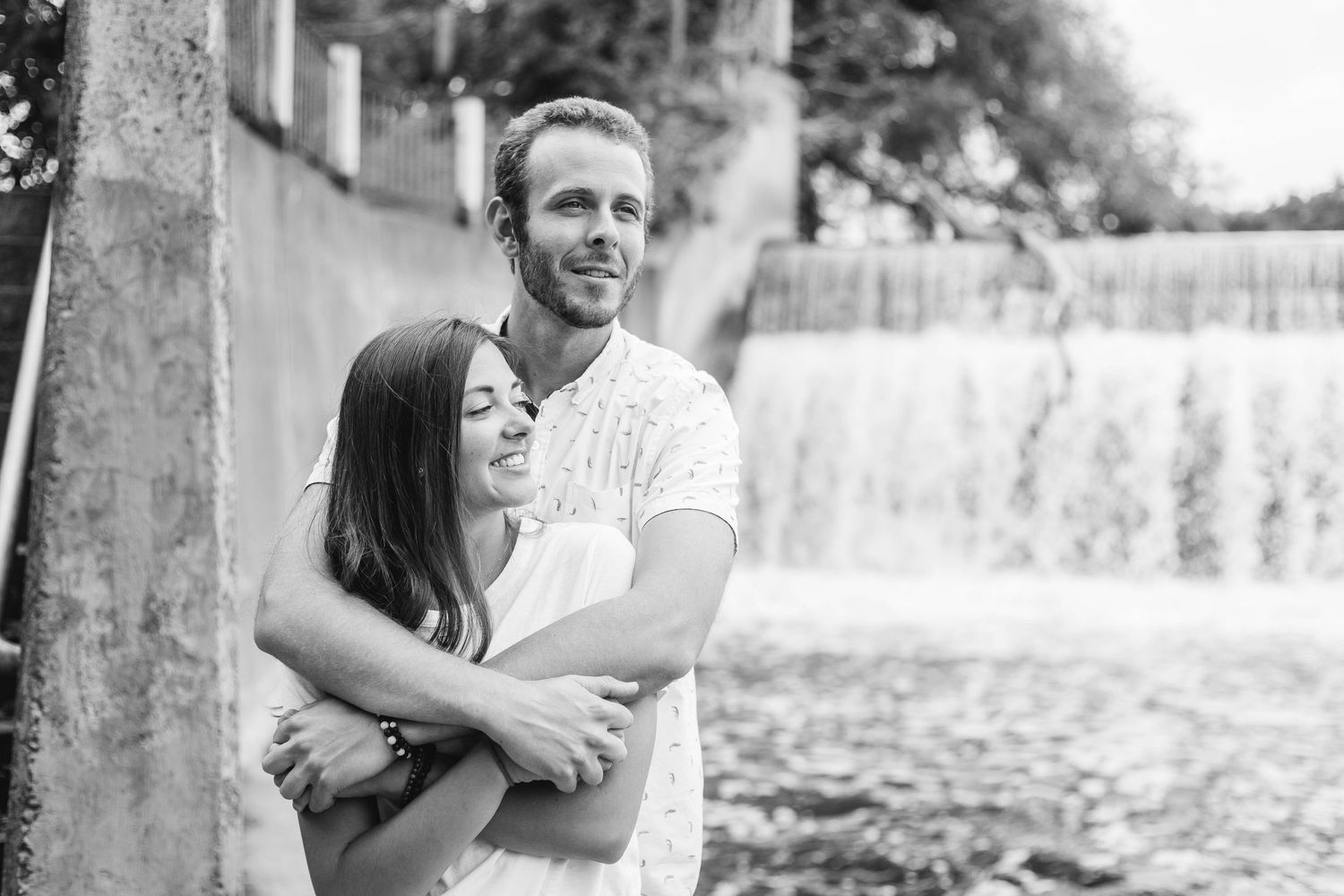 A couple shares a romantic embrace near a waterfall in a classic black and white engagement photo.
