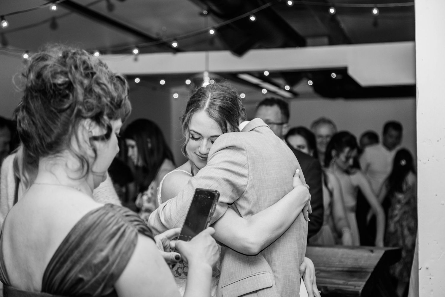 Black and white photo of bride sharing a warm embrace with a guest at wedding reception.