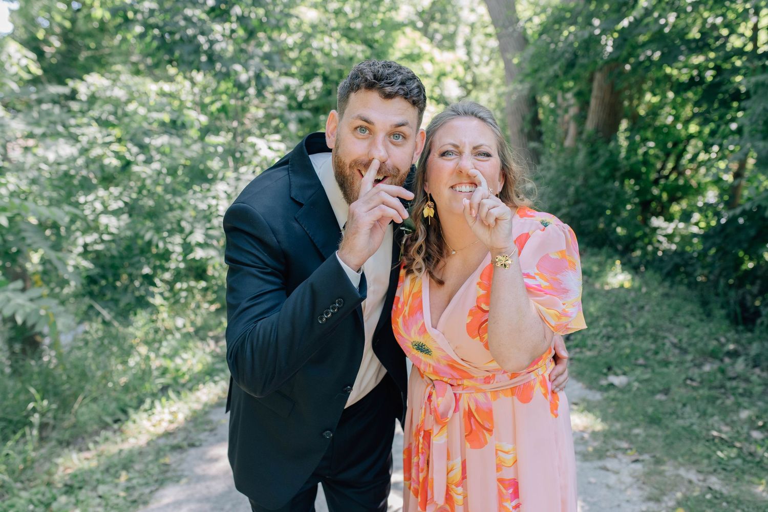 Joyful man in a suit and woman in a floral dress laughing while re-creating a childhood photo along a trail in Paris Ontario.