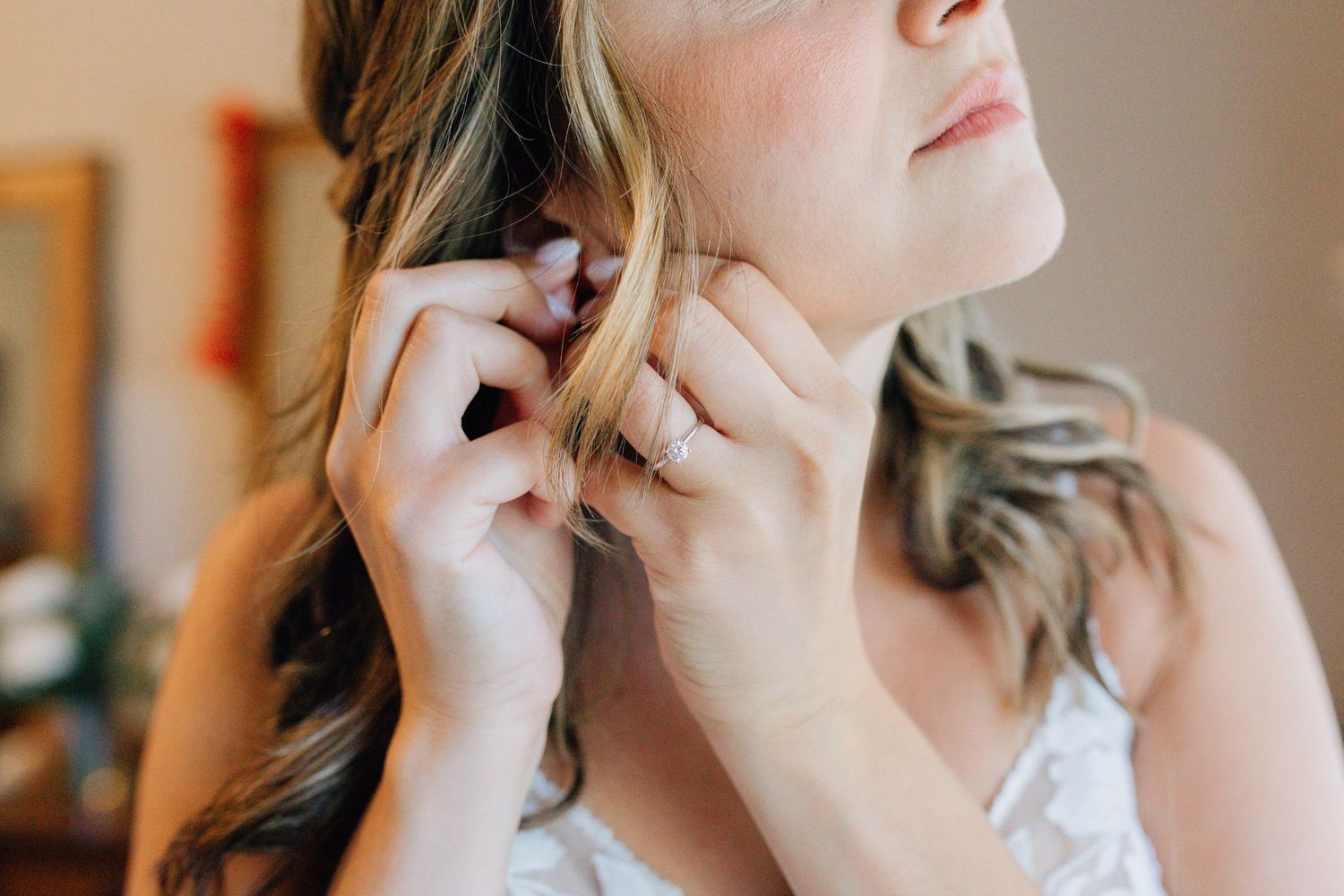Close-up of bride putting on elegant earrings while wearing a lace wedding dress.